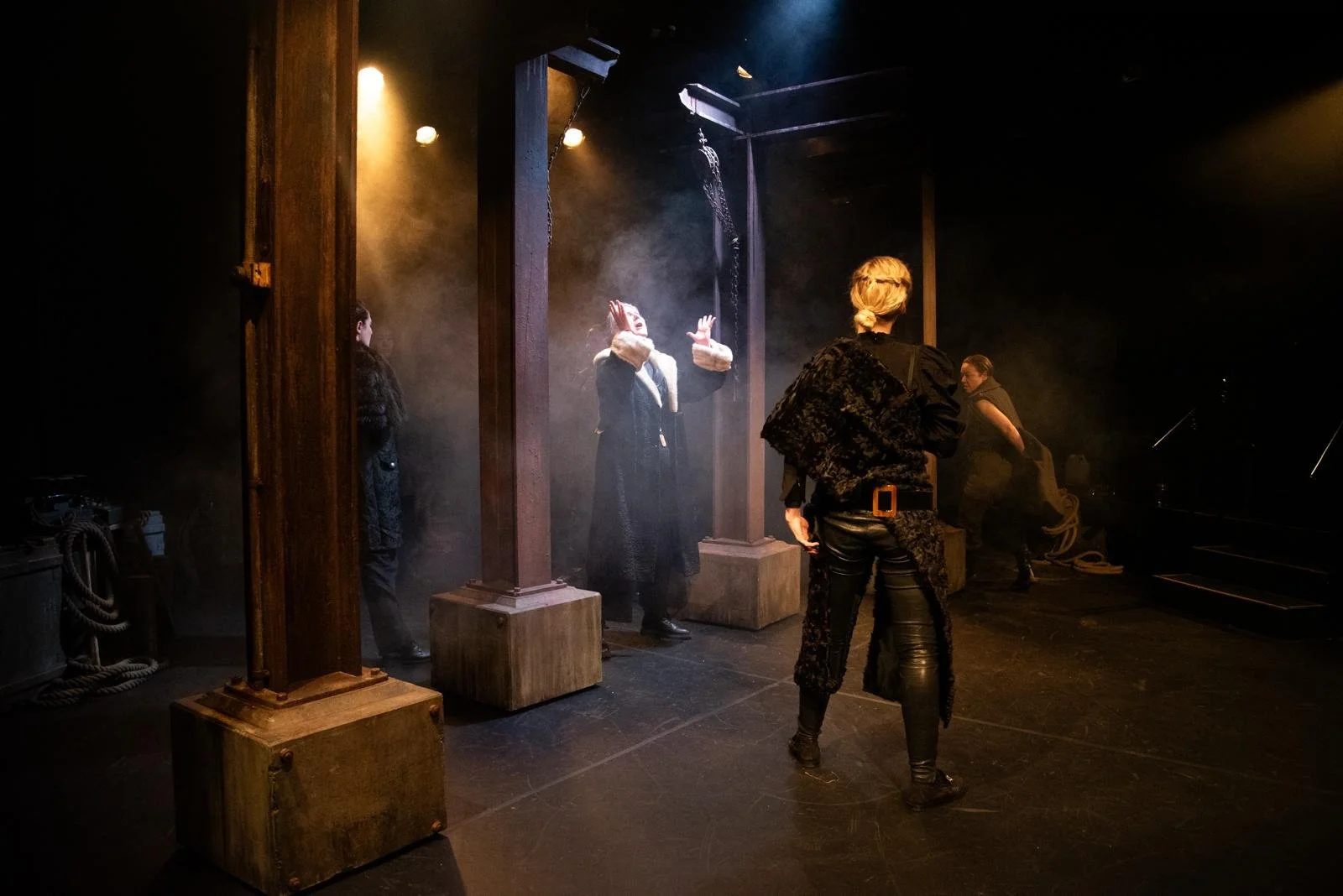 People rehearsing or performing on a stage with wooden columns and smoky atmosphere, with warm tissue lighting