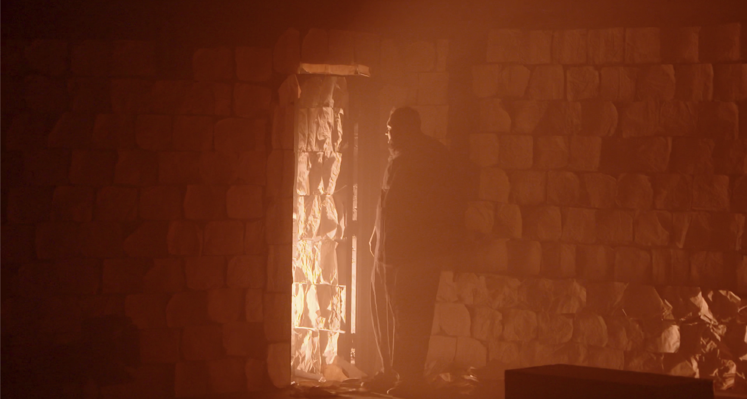 Person standing inside a stone-walled room, looking at a window with bright sunlight shining through.