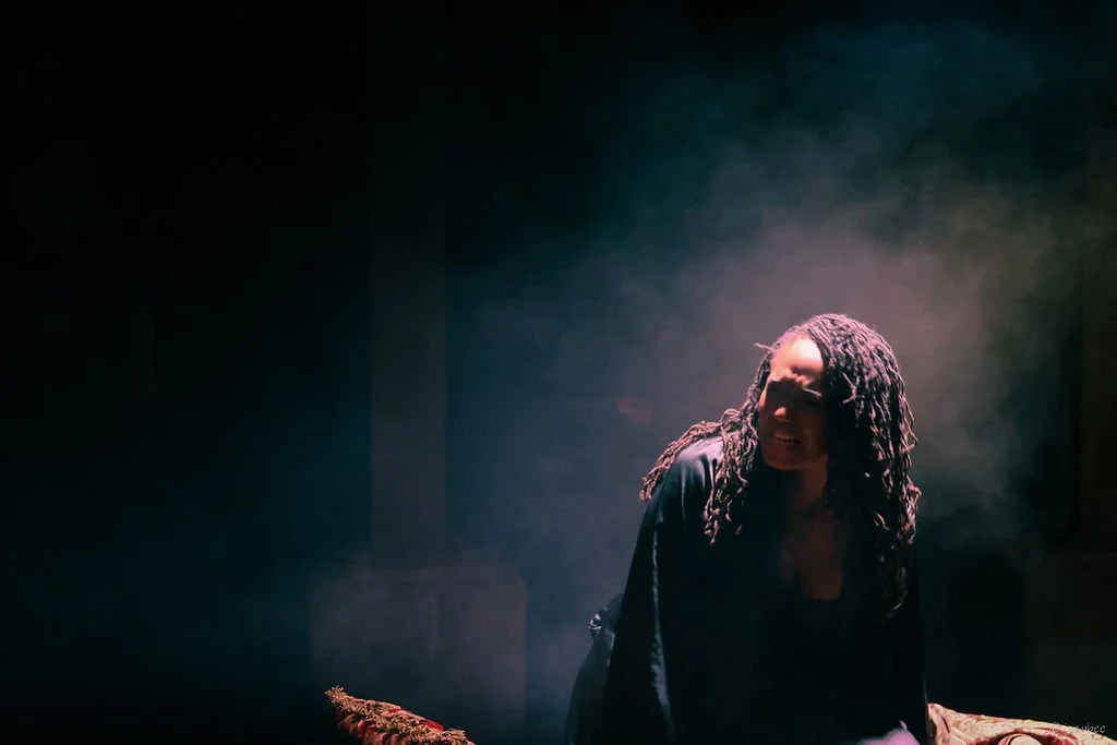 A woman with dreadlocks looking distressed in a smoky, dark room.