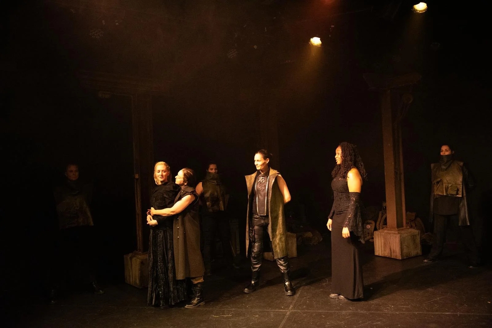 Actors on stage performing in a theatrical play with dim lighting and minimal props.