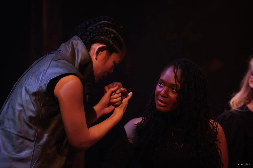 Two women engaging in an intense arm wrestling match, with one woman pulling the other's hand and the other woman looking on with a serious expression.