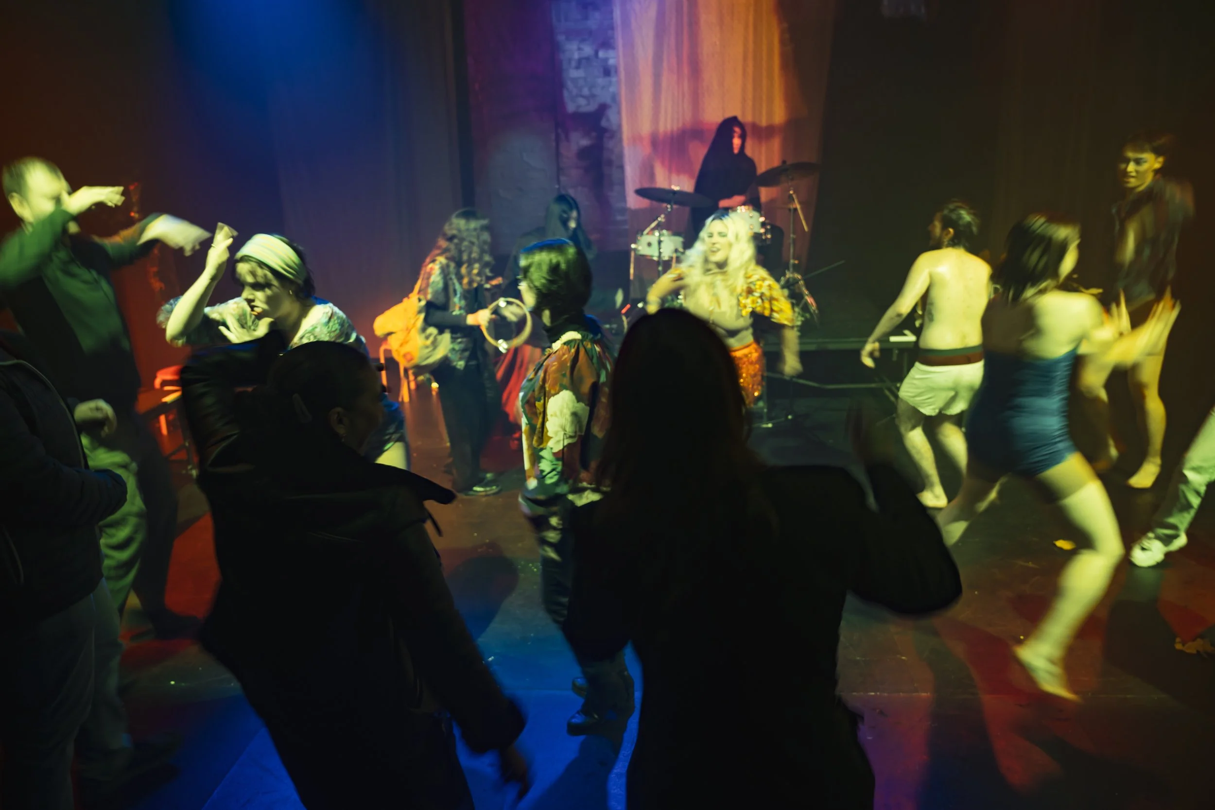 People dancing and enjoying drinks at a lively indoor party with a live band playing on stage in the background.