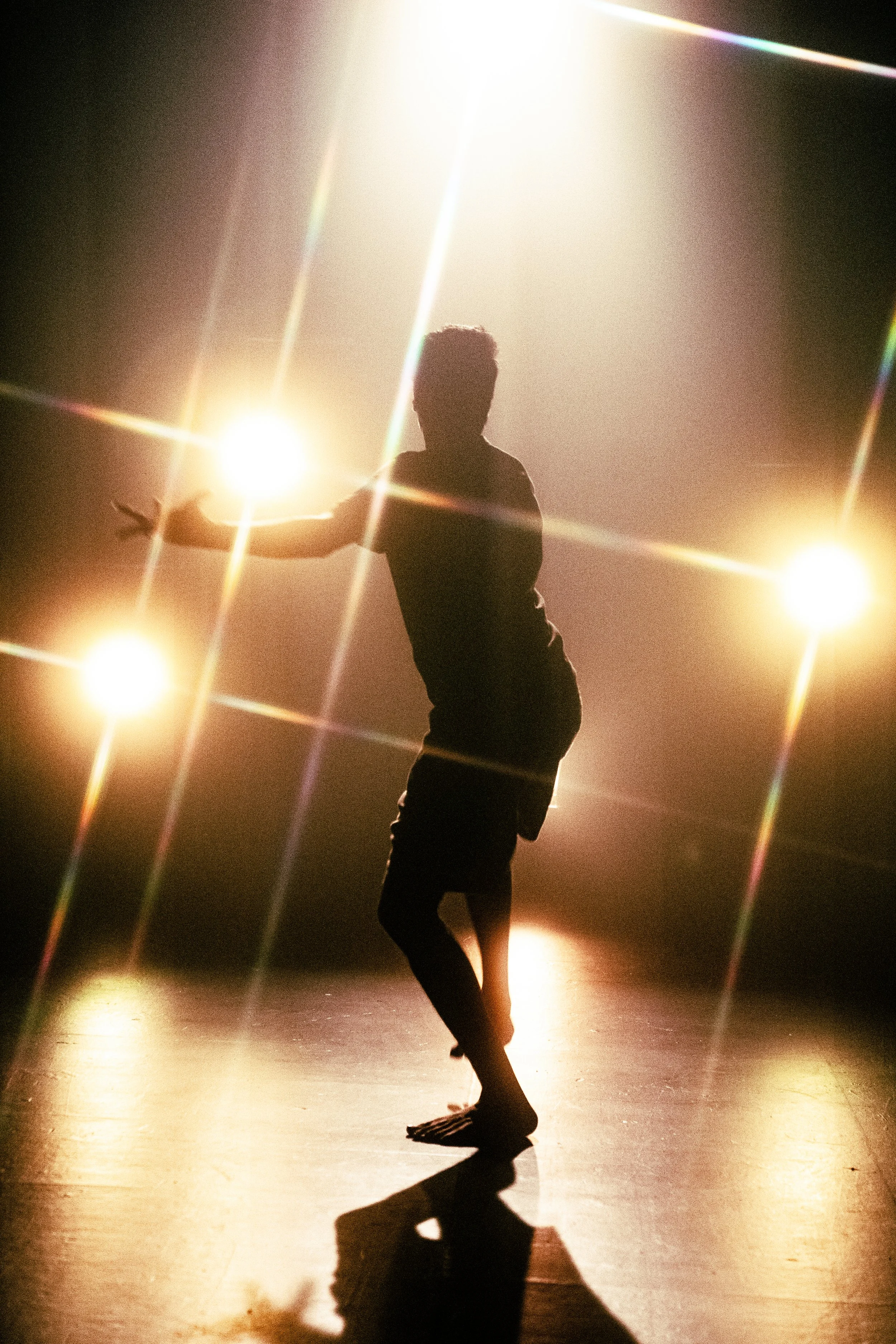 A silhouette of a person dancing on stage with bright lights creating a starburst effect around them.