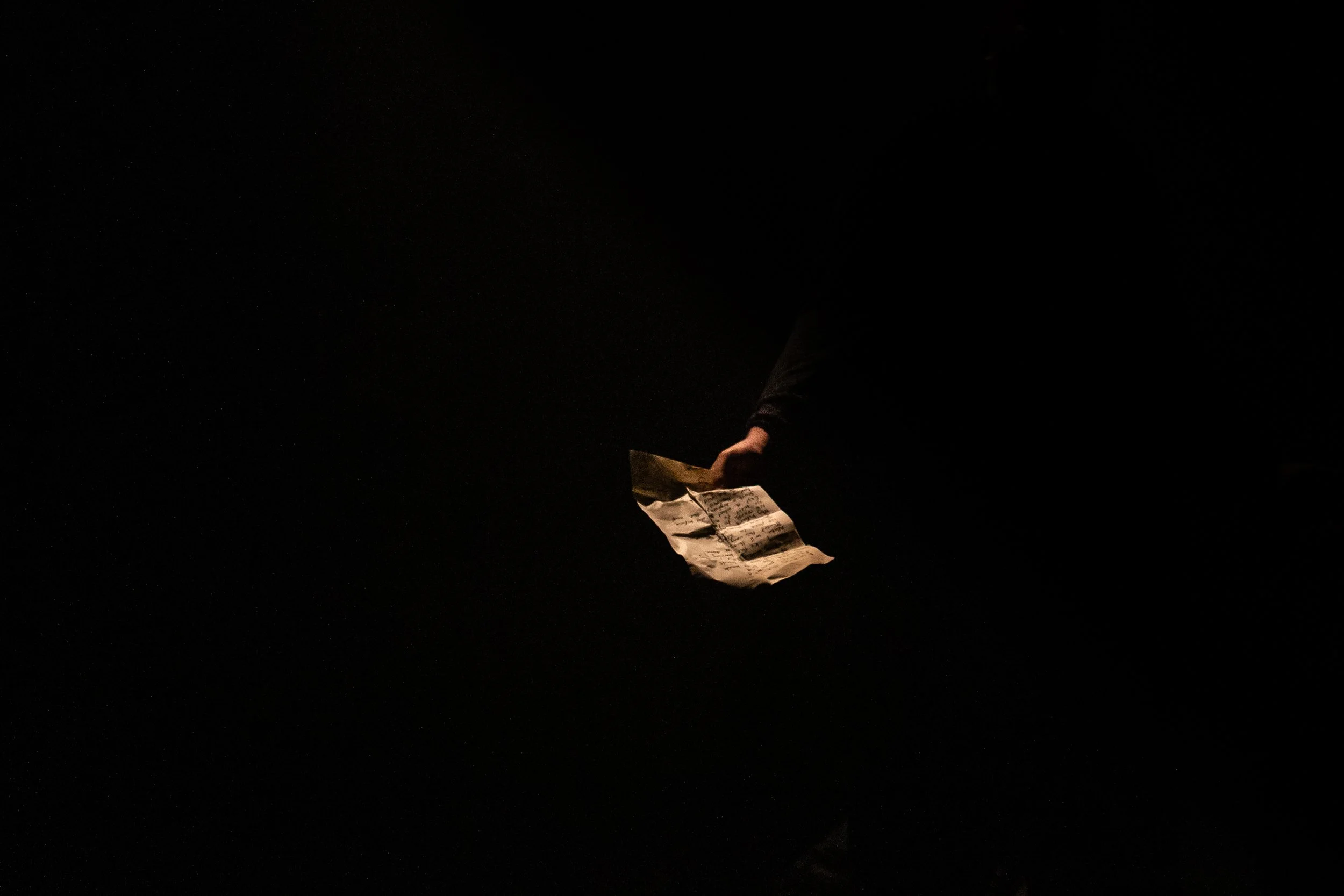 A person holding a crumpled piece of paper in a dark environment, with only their hand and part of their sleeve visible.