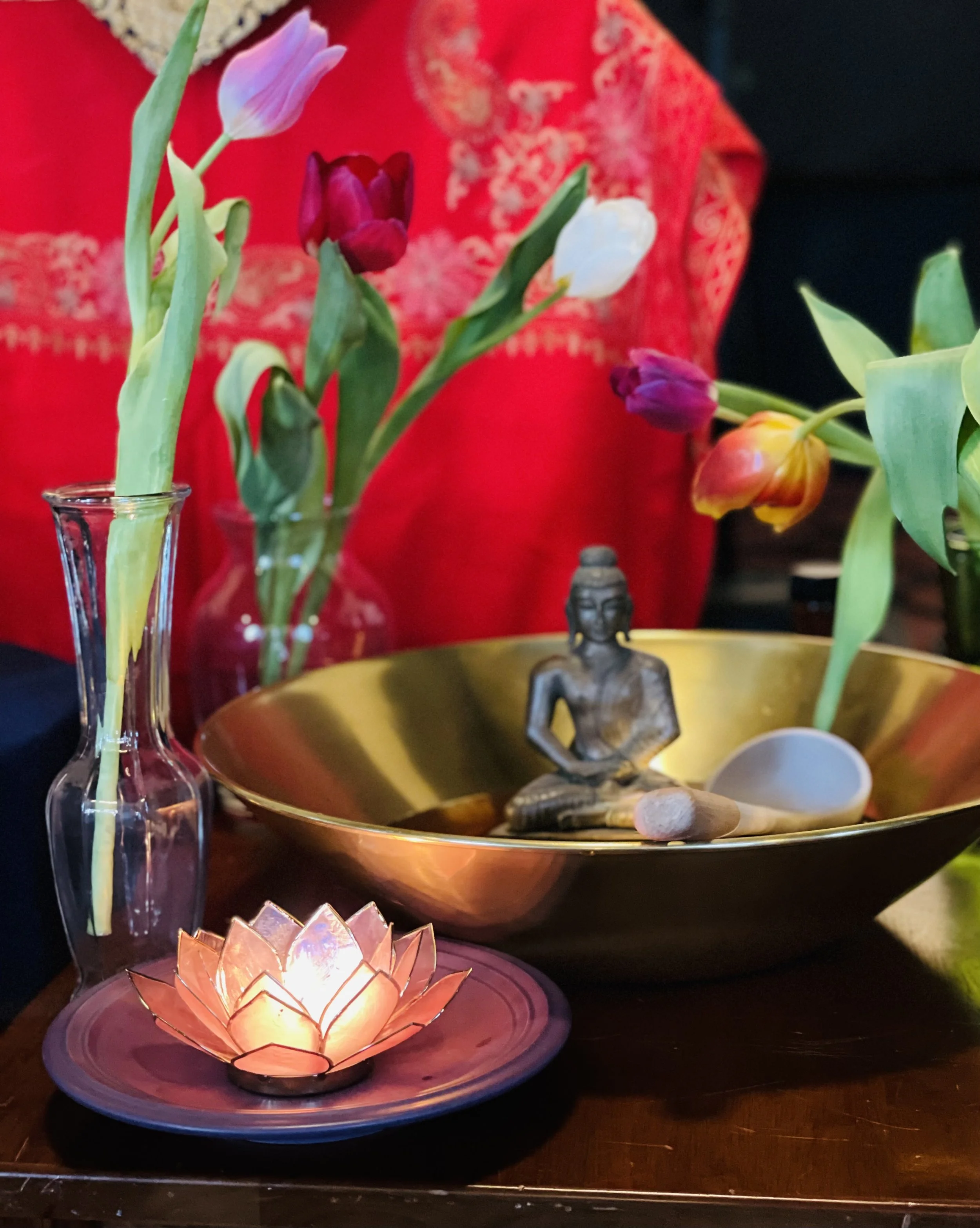 Vase with tulips, a golden bowl with a Buddha statue, a small candle, and a white spoon on a table.