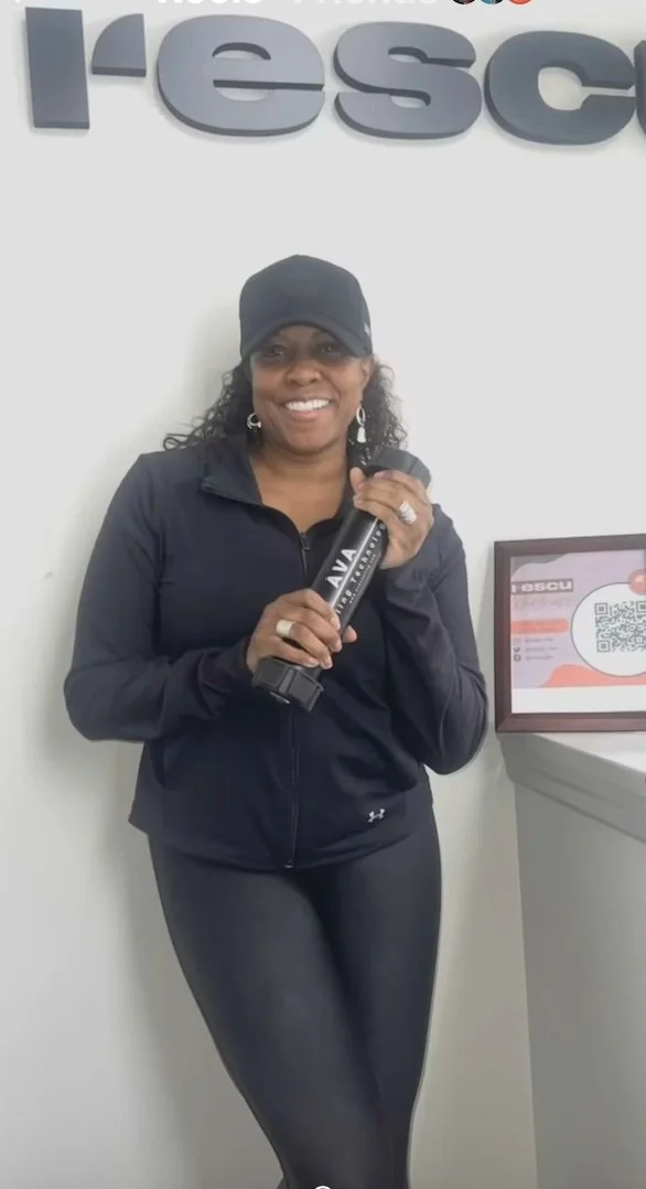 A woman with dark hair in a ponytail wearing a dark-colored jacket standing in front of a brick wall.