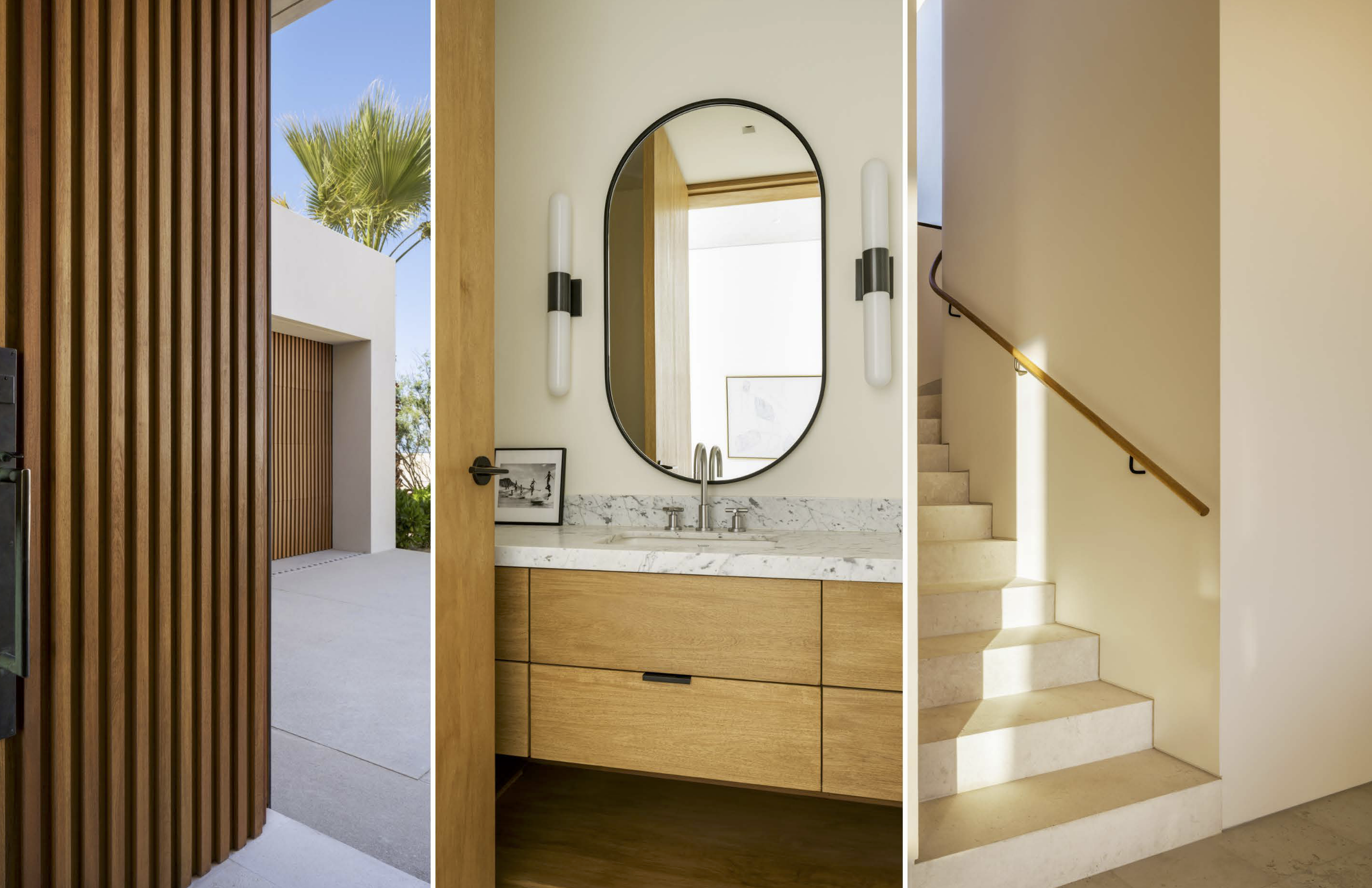 A modern interior view of a bathroom with a marble countertop, wooden cabinets, an oval mirror, two wall-mounted light fixtures, a staircase to the right, and an entrance to an outdoor area with a palm tree visible.