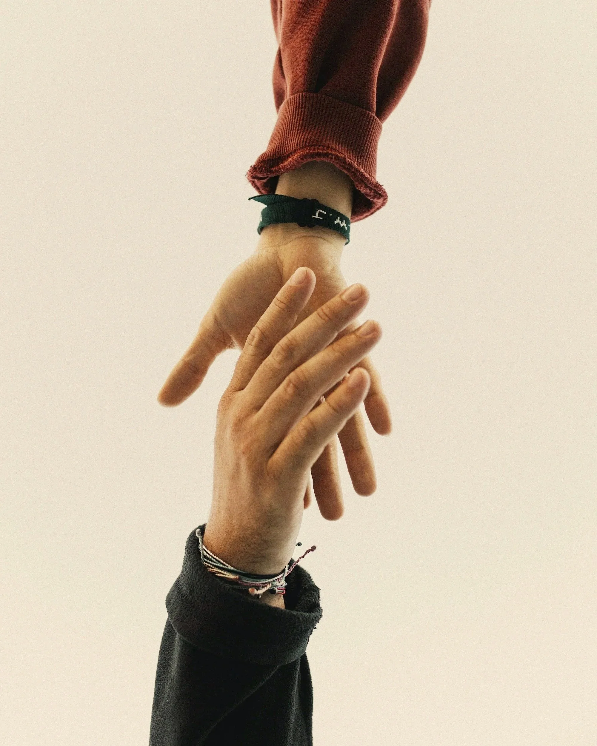 One person’s hand holds another person’s hand in a gentle grip against a plain white background.