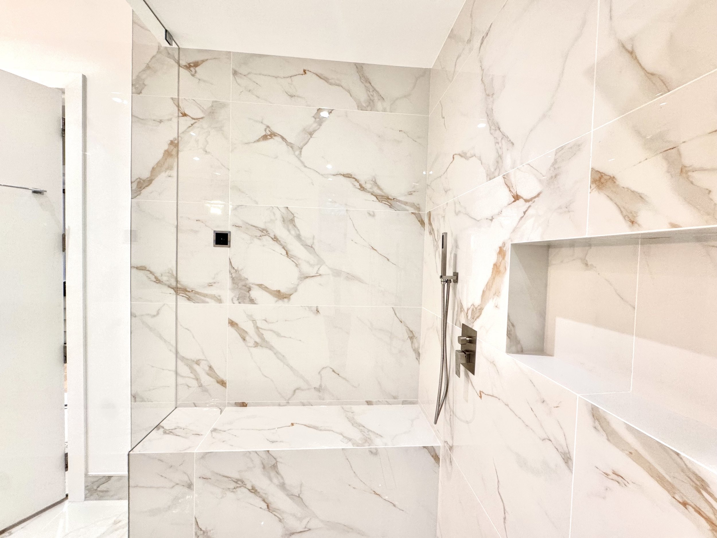 Modern shower with white marble tiles featuring brown and gray veining, built-in niche, and a wall-mounted showerhead.
