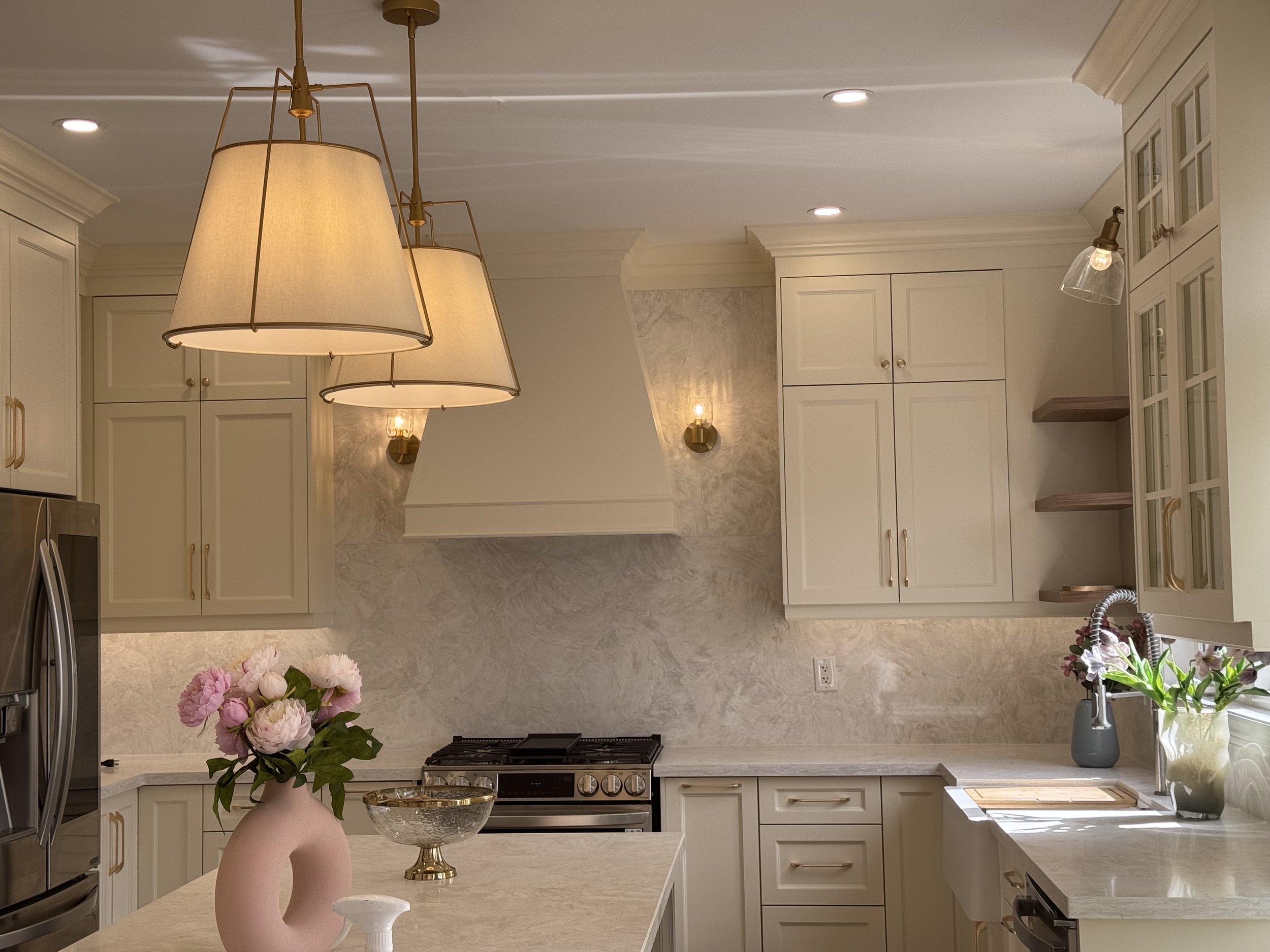 Modern kitchen with white cabinets, marble countertops, a stove, stainless steel appliances, and a center island with pink flowers in a white vase.