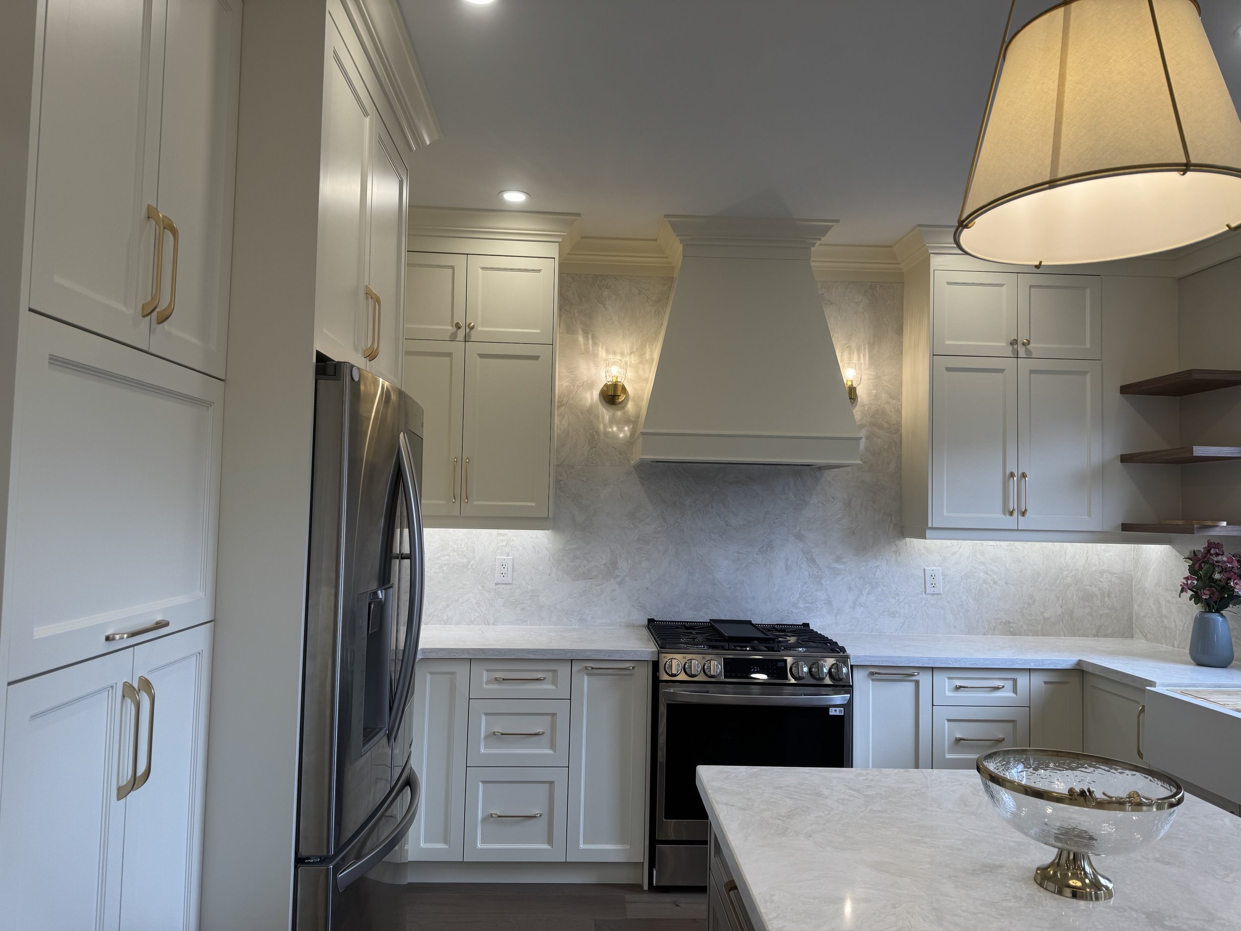 Modern kitchen with white cabinets, marble countertops, stainless steel refrigerator, and a gas stove, decorated with a vase of flowers and a glass bowl on the counter.