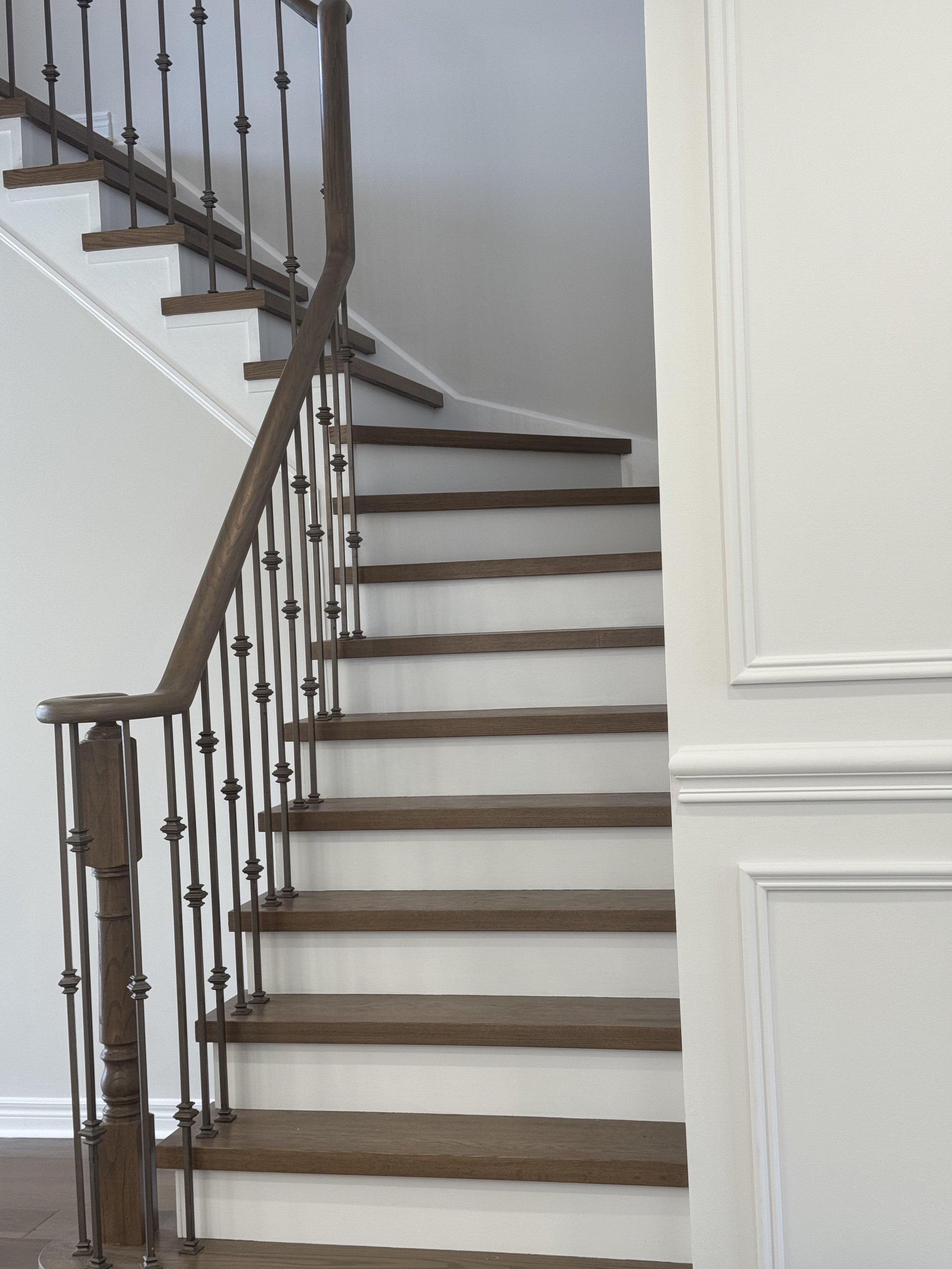 Wooden staircase with metal railing and white walls.