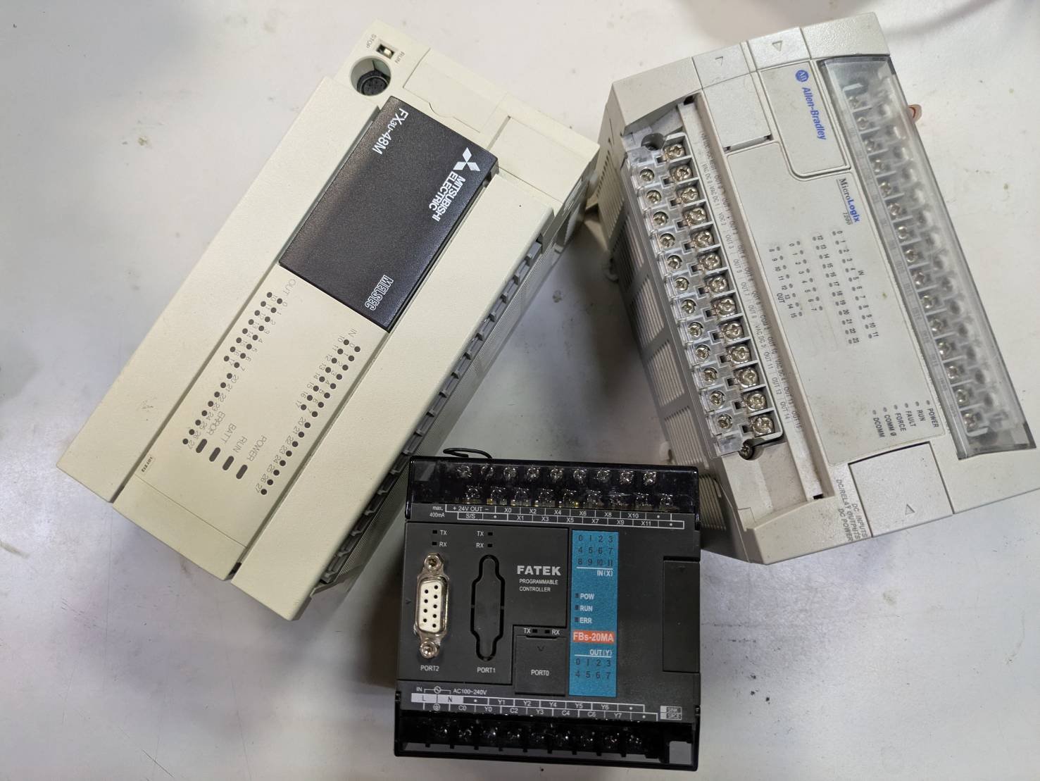 Various industrial control components, including a Mitsubishi relay, a Allen-Bradley terminal block, and a FATEK programmable controller on a white surface.