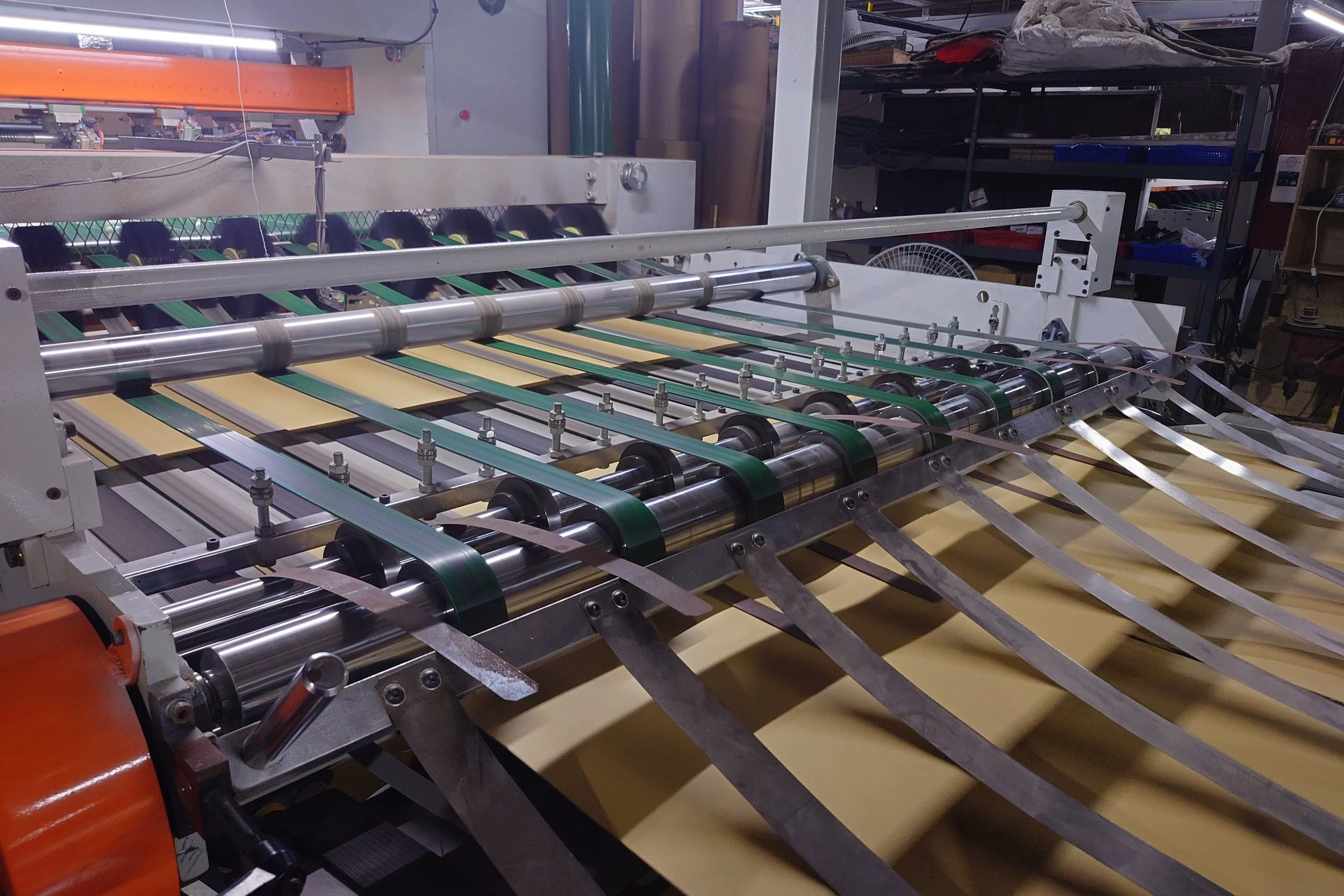 Industrial manufacturing machine on production line handling multiple green and beige strips of material, with rollers and metal rods, in a factory setting.