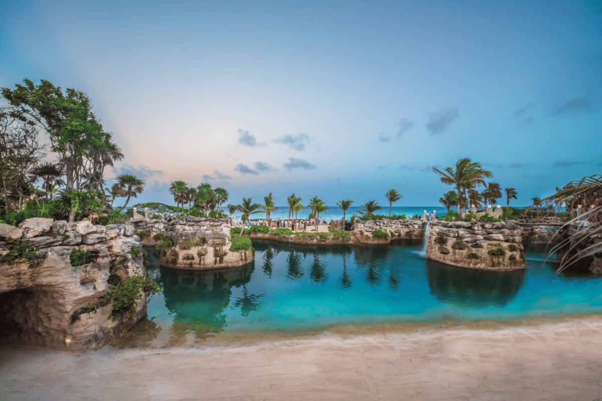 Lagoon-style beach and crystal clear water at Hotel Xcaret Mexico with tropical landscaping and palm trees