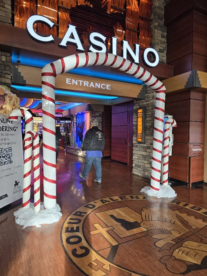 Entrance to a casino decorated with large candy cane props and a festive holiday theme, with the casino logo on the floor.