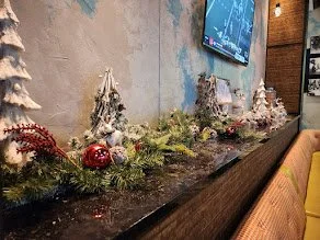 Holiday decorations on a bar counter with small snow-covered trees, red ornaments, and greenery.