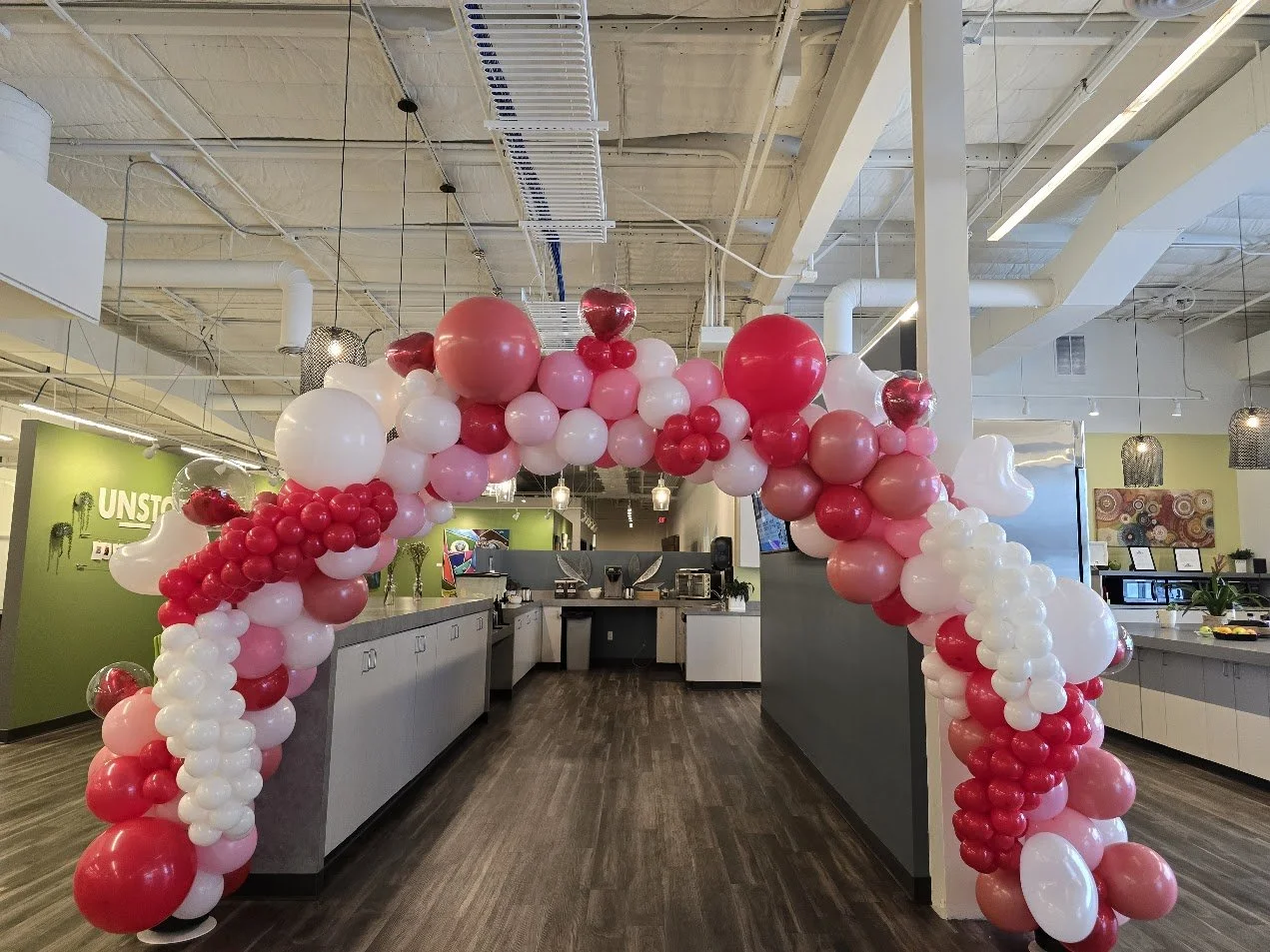 Decorative balloon arch made of pink, white, red, and maroon balloons in an indoor cafe or restaurant space.
