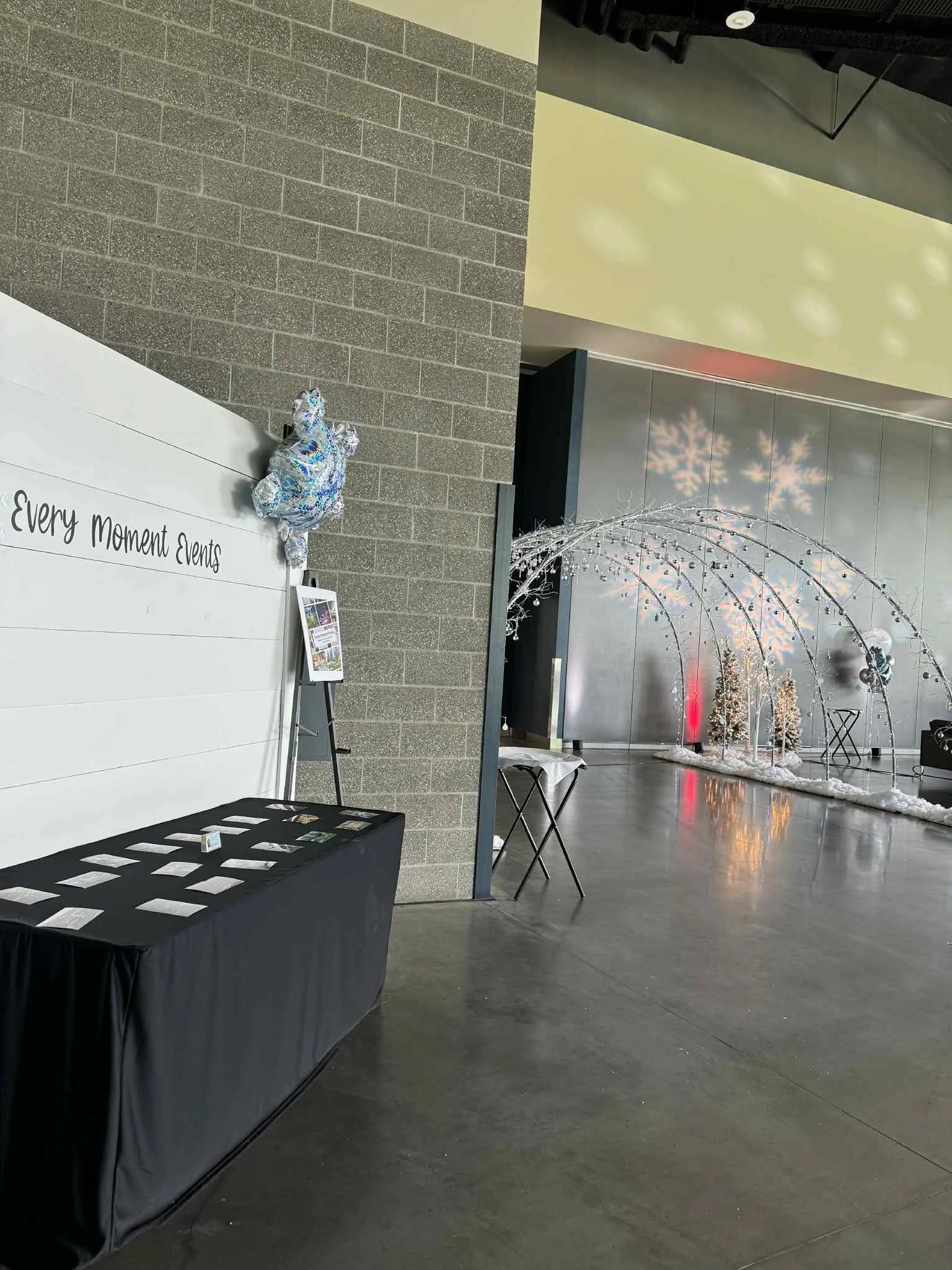 Indoor holiday display with a decorative arch, snow-like decorations, Christmas trees, and snowflake projections on the wall.