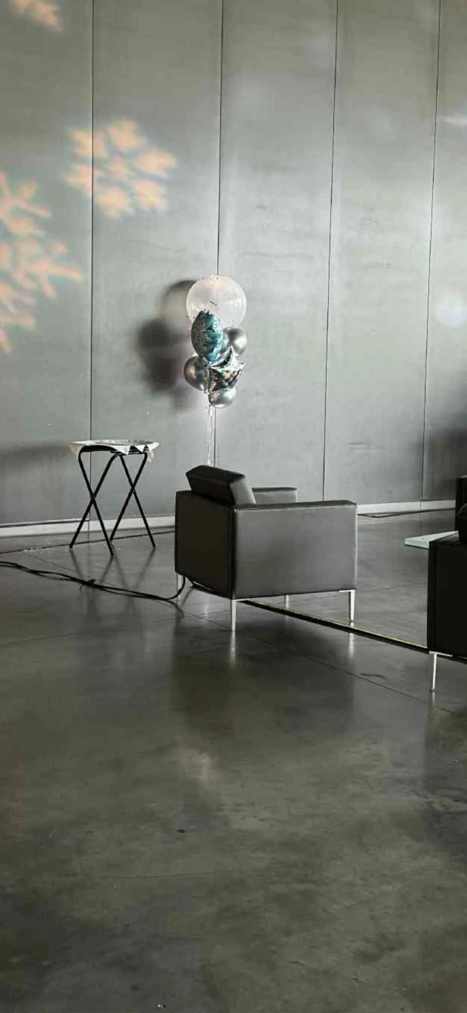 Empty modern lounge with gray armchair, small table, and a bunch of balloons with a number 8 and planets, near gray wall and concrete floor.
