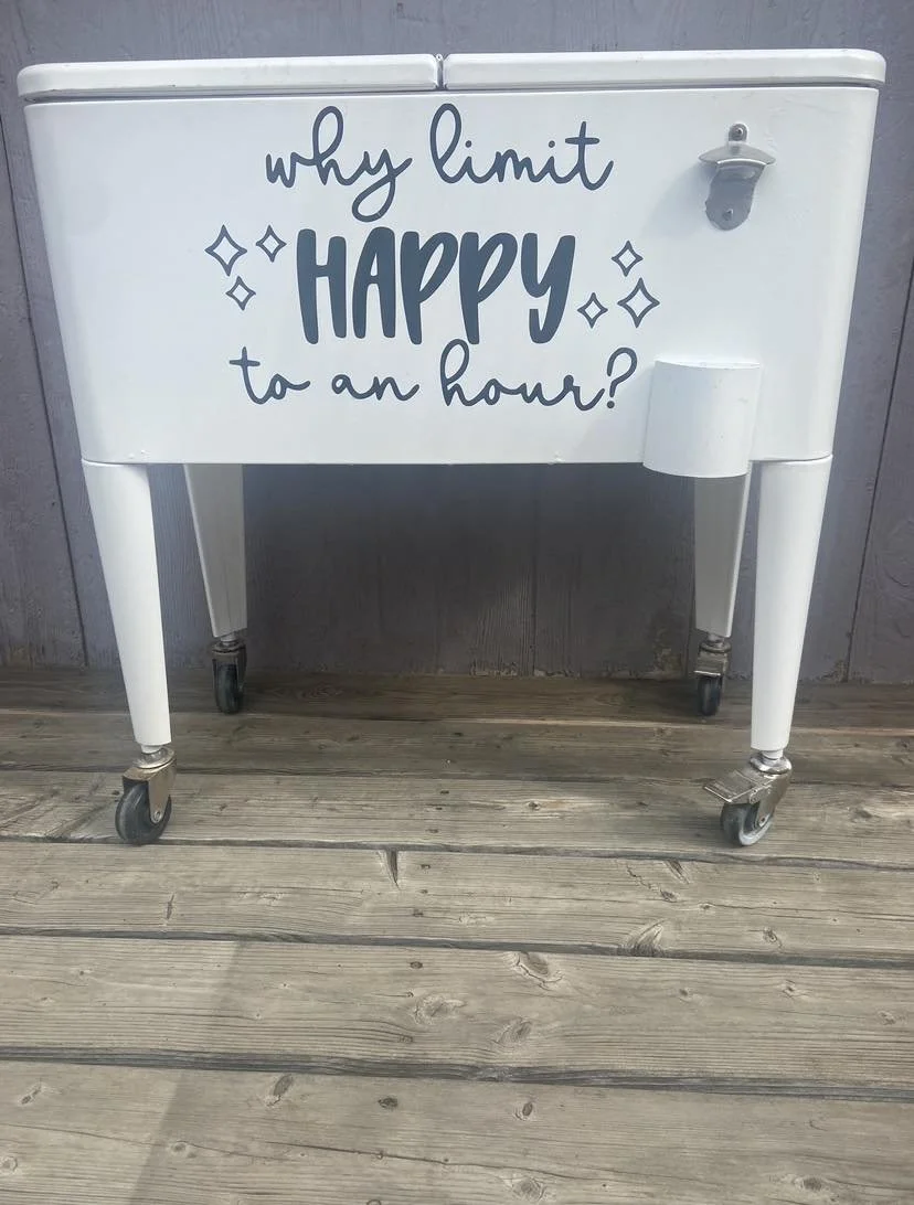 White rolling cart with the message "Why limit happy to an hour?" written in blue text, sitting on a wooden floor against a gray wall.