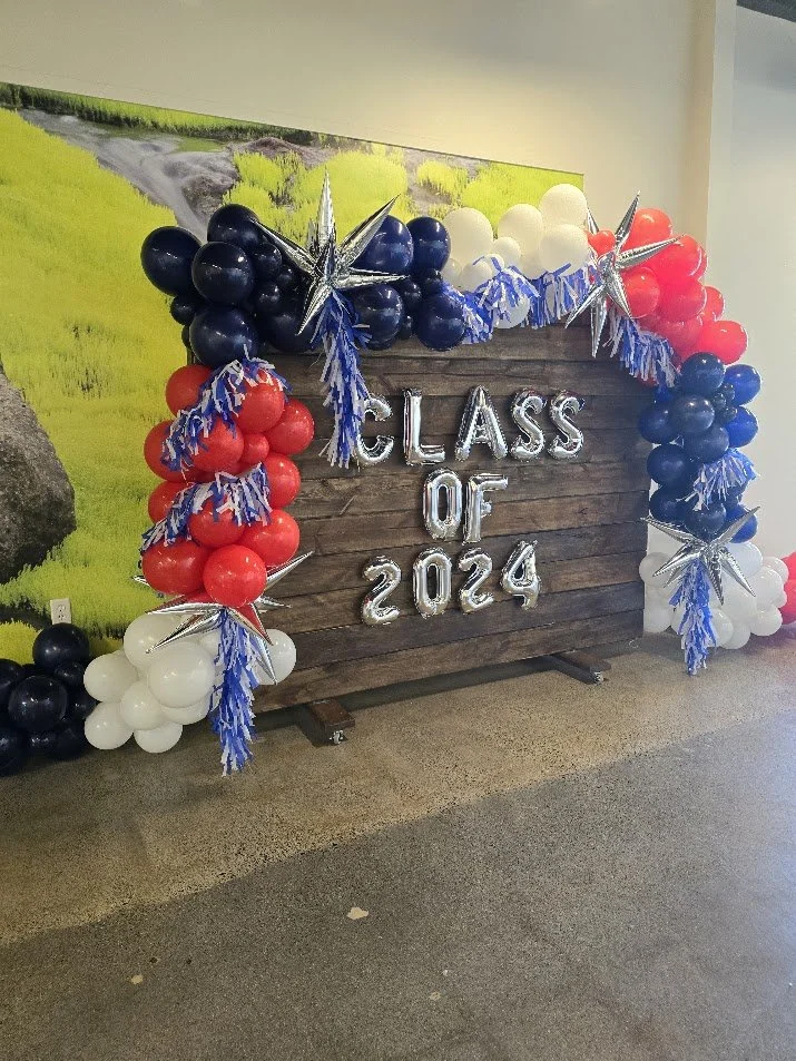A decorative display for graduation with balloons and a wooden sign that reads 'Class of 2024'.