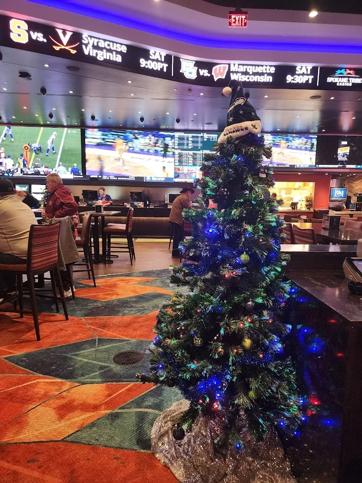 Small decorated Christmas tree with lights, ornaments, and a Santa hat on top, in a sports bar. There are TVs and patrons in the background.