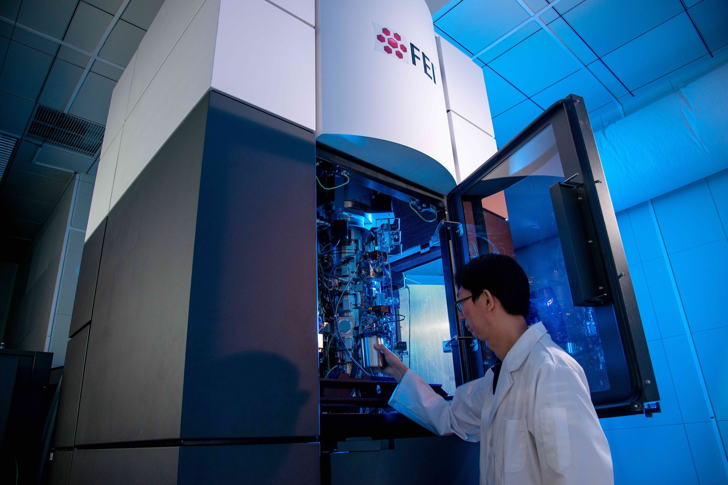 Scientist in a white lab coat examines a large scientific machine with the FFI logo in a high-tech laboratory.