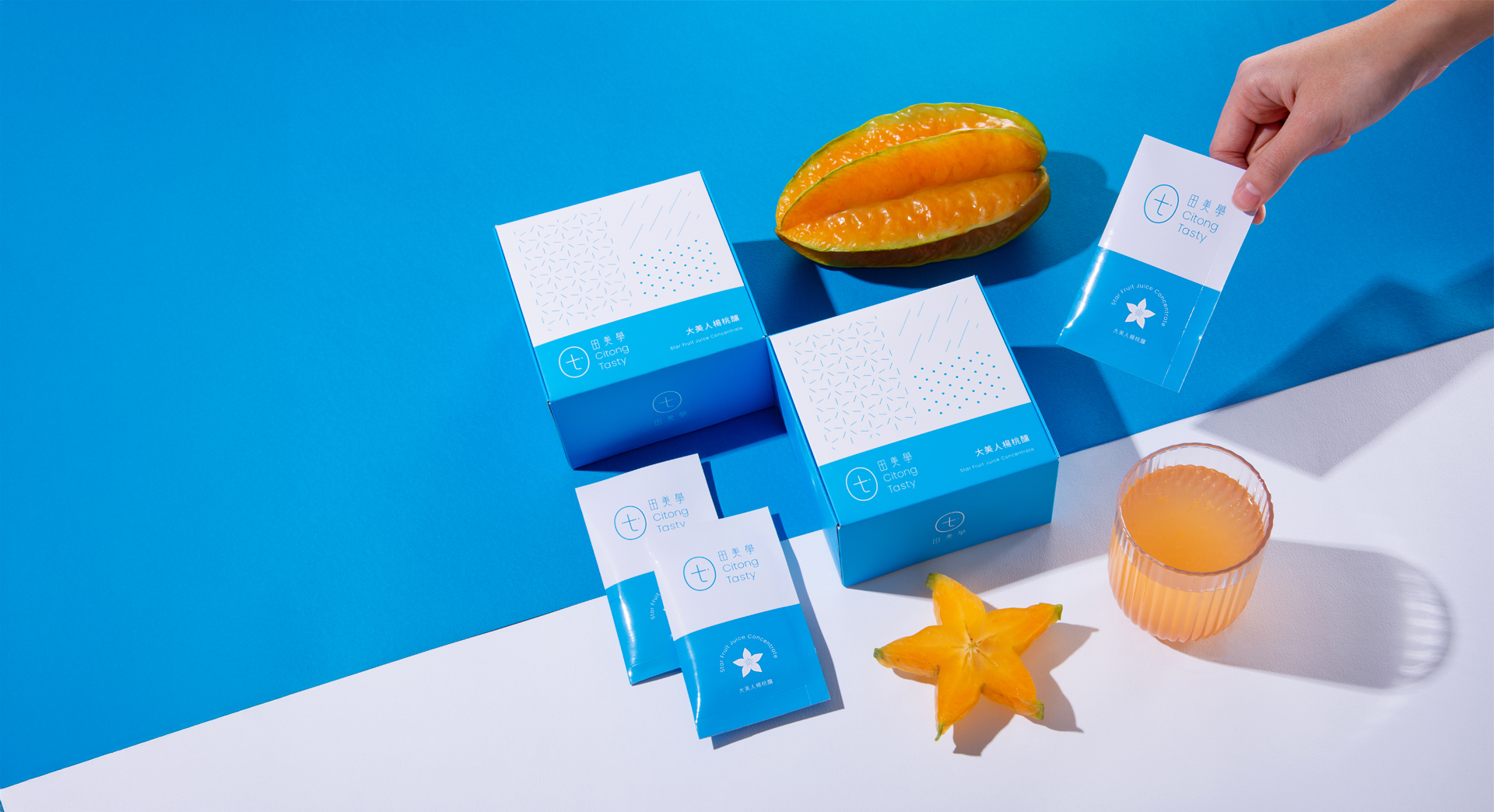 Blue and white packaging boxes labeled 'Citong Tasty' on a two-toned blue and white background with half a starfruit, a glass of orange juice, and a whole starfruit.