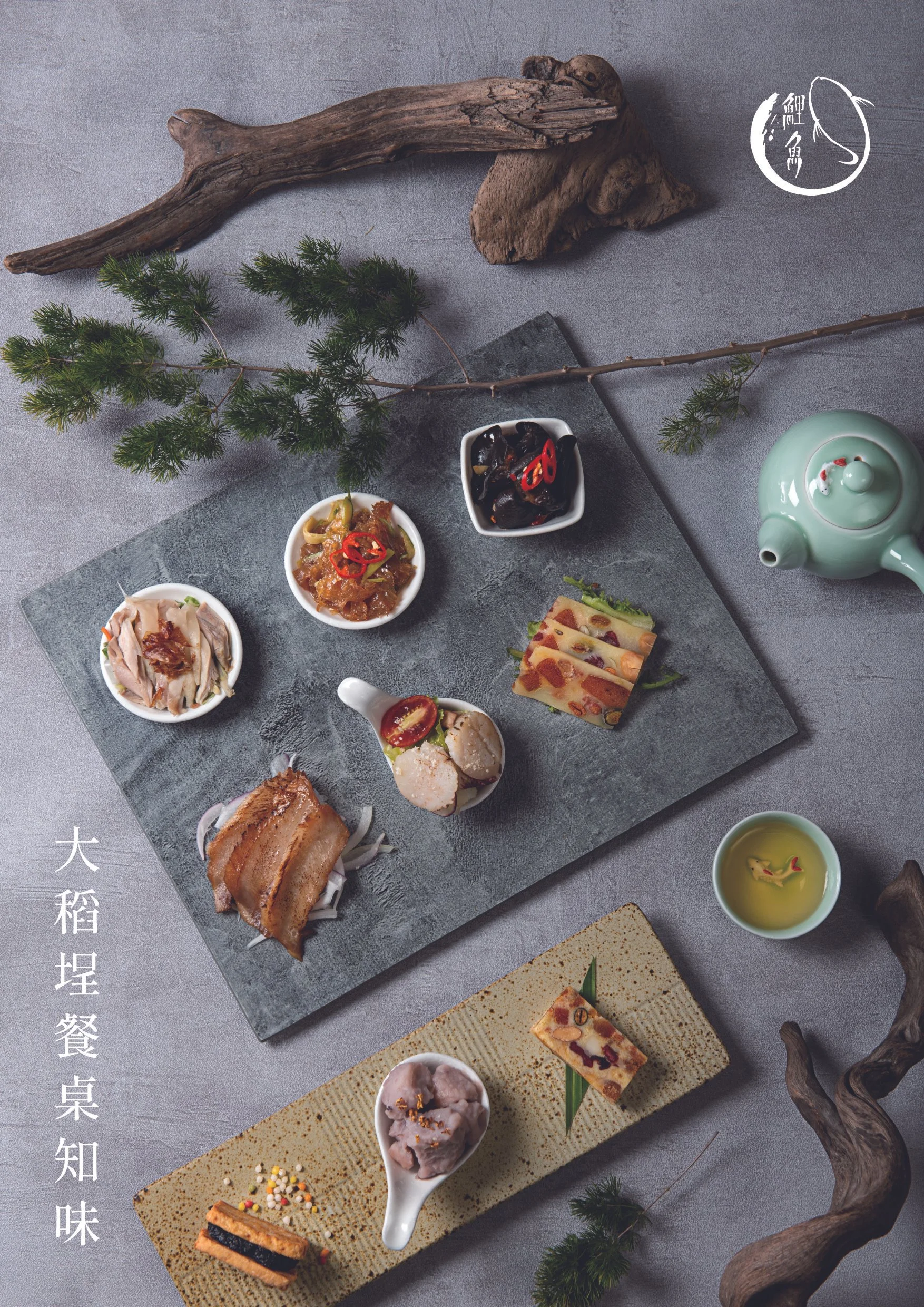 A traditional Chinese appetizer platter with various small dishes served on a black slate and a beige rectangular plate, surrounded by decorative natural elements like driftwood and pine branches, and a green teapot and teacup.