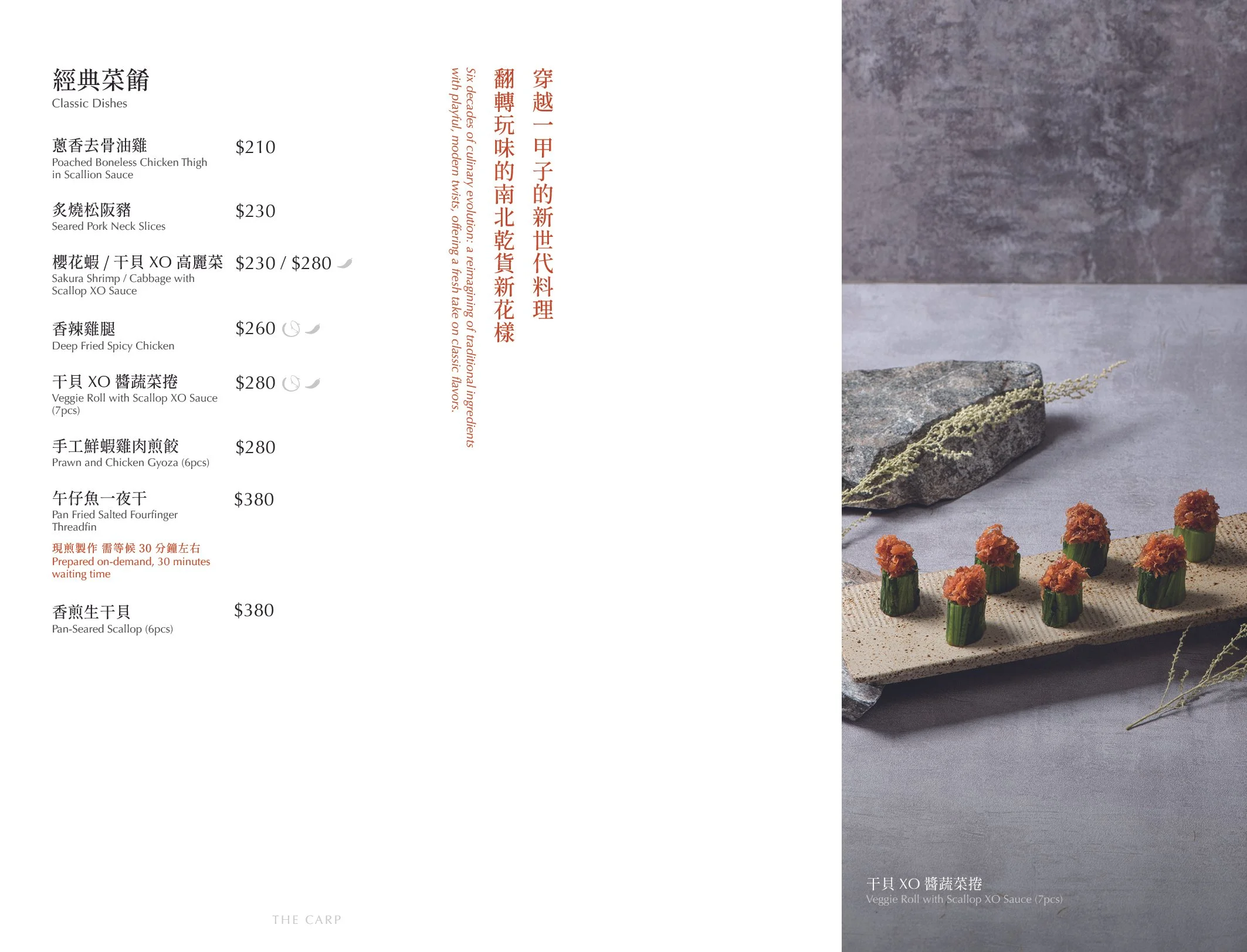 A menu page listing classic dishes with descriptions and prices in Chinese and English, alongside a photo of a plate of veggie rolls topped with Scallop XO sauce, arranged on a beige rectangular platter with decorative stones and plants in the background.