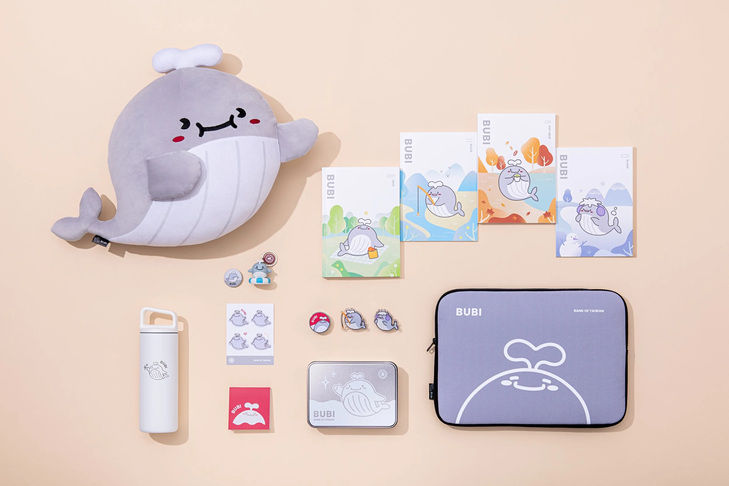 Collection of whale-themed items including a large whale plush, three illustrated whale postcards, three whale pins, a small whale figurine, a whale button, a set of whale stickers, a white water bottle with whale illustration, a silver tin box with whale illustration, a gray zippered bag with whale design, and a small note card with whale illustration, all arranged on a beige background.