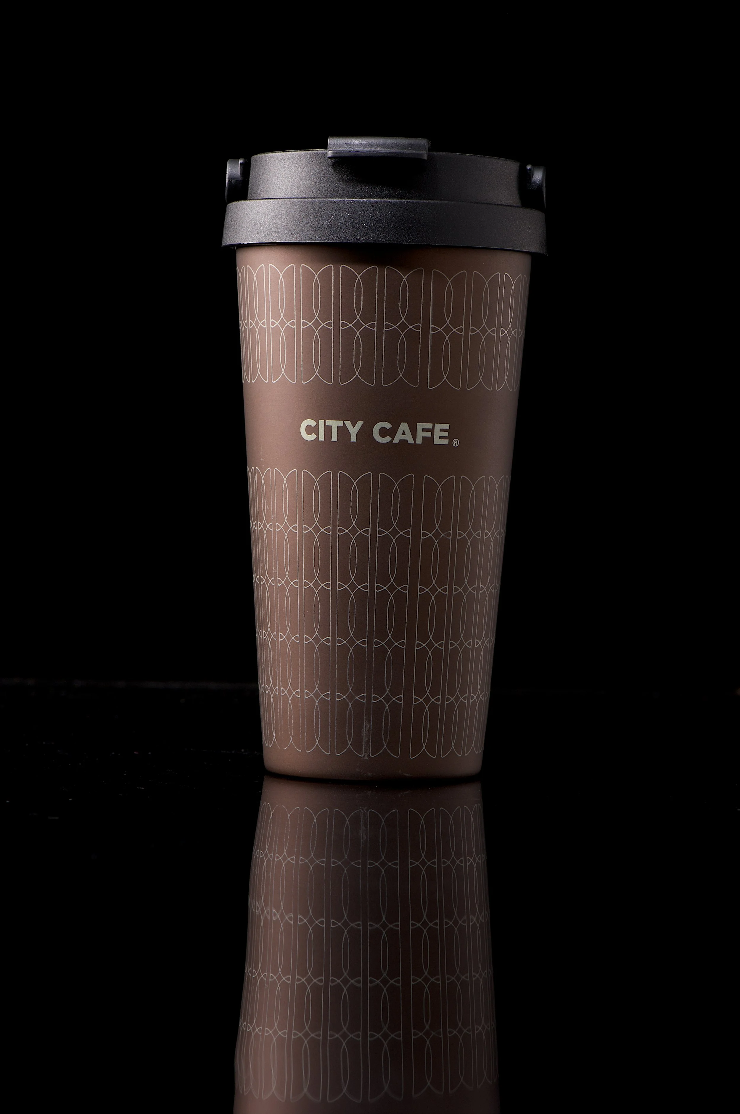 A disposable coffee cup with a black lid, branded with 'CITY CAFE' on a black reflective surface and dark background.