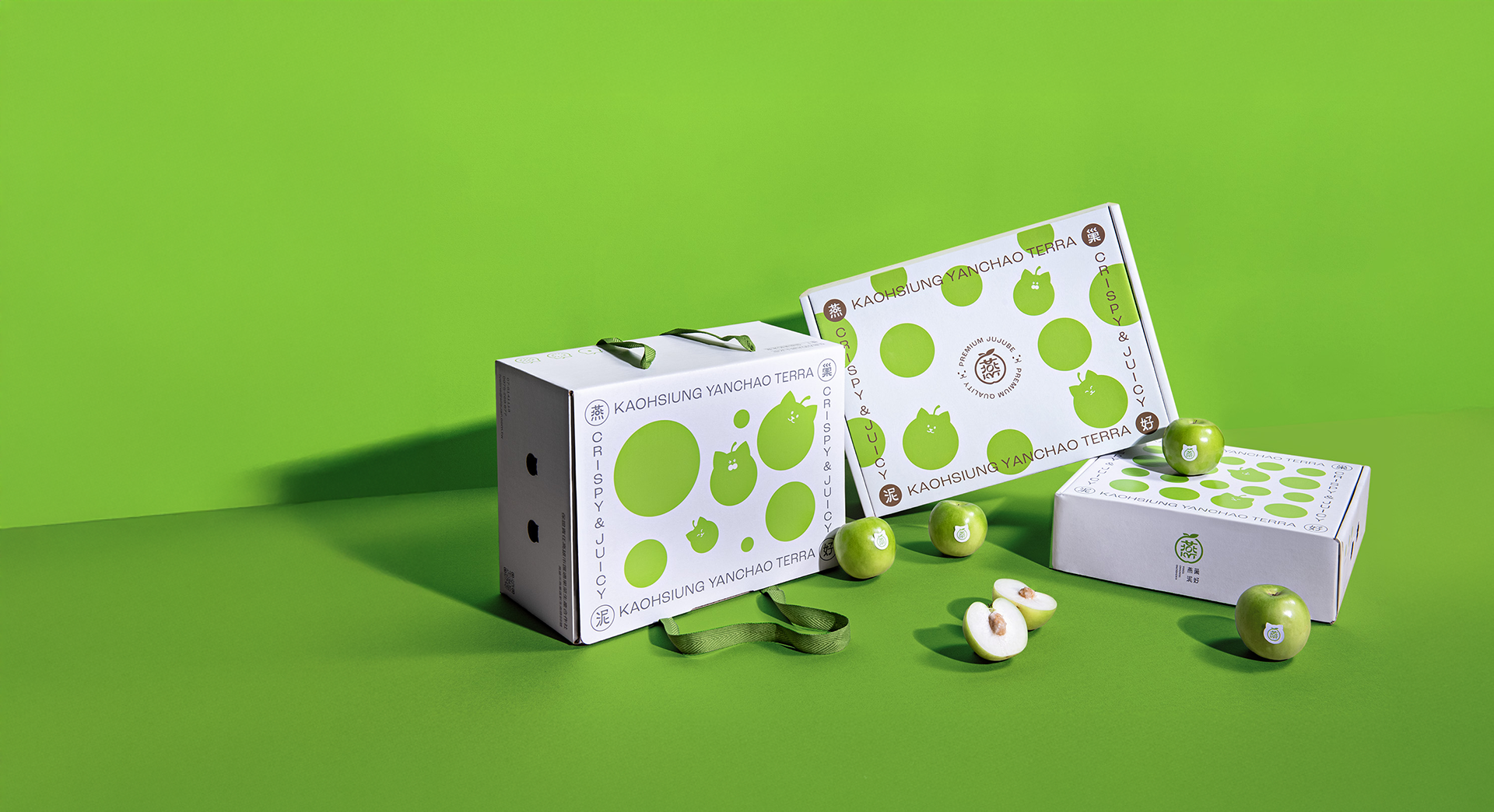 Various green packaging boxes and artificial green apples with white and green labels on a green background, some apples cut in half showing the seeds inside.