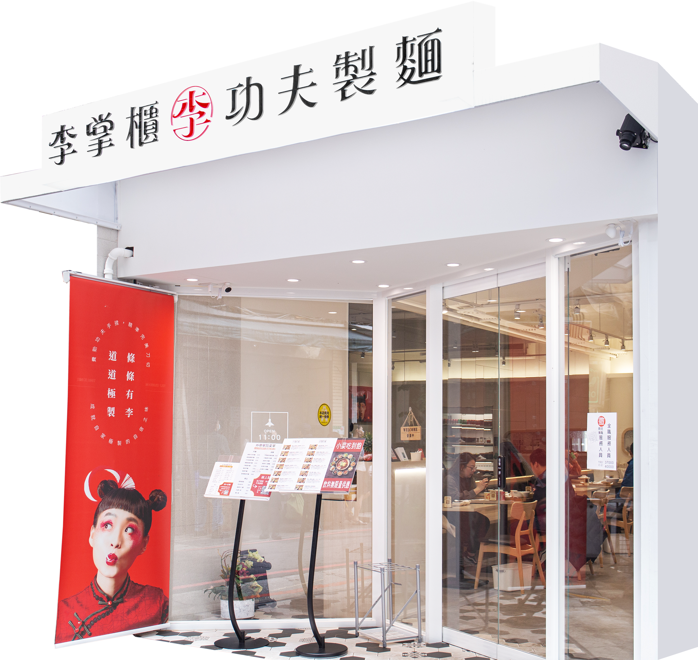 Exterior of a Chinese restaurant with large glass windows and a white facade. Sign with Chinese characters and a red logo is displayed at the top. A red vertical banner with a woman's face and more Chinese characters stands outside, along with a menu stand showing restaurant offerings.