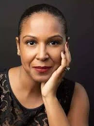 Portrait of a person posing with hand on chin against a dark background.