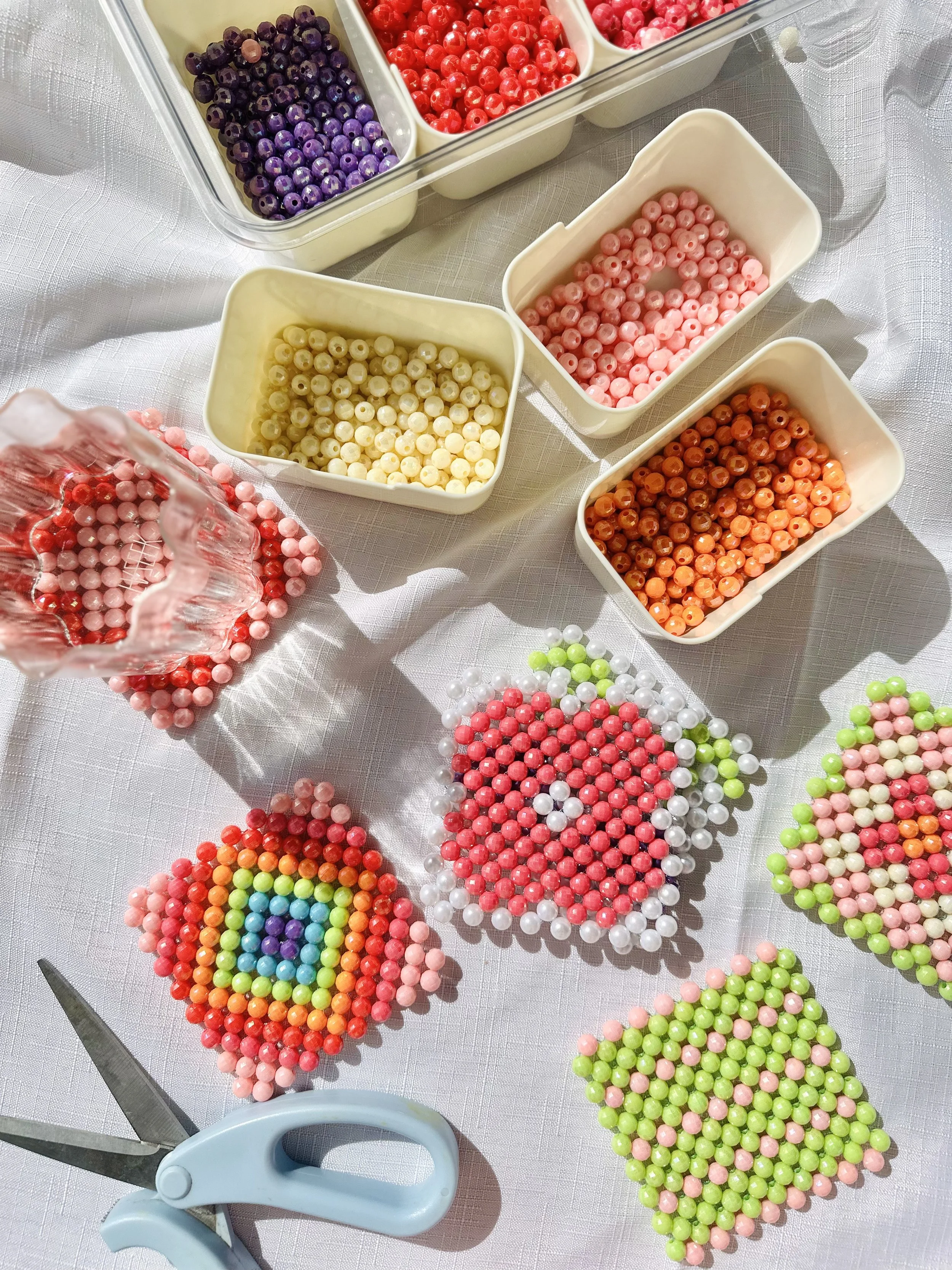 Colorful beads arranged in piles and containers on a white table with scissors nearby.