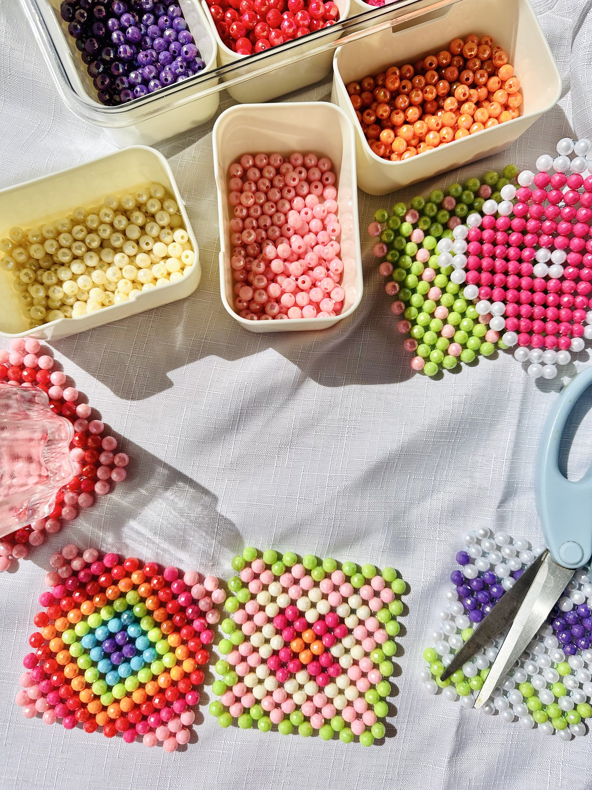 Colorful beads in various containers and scattered on a white tablecloth.