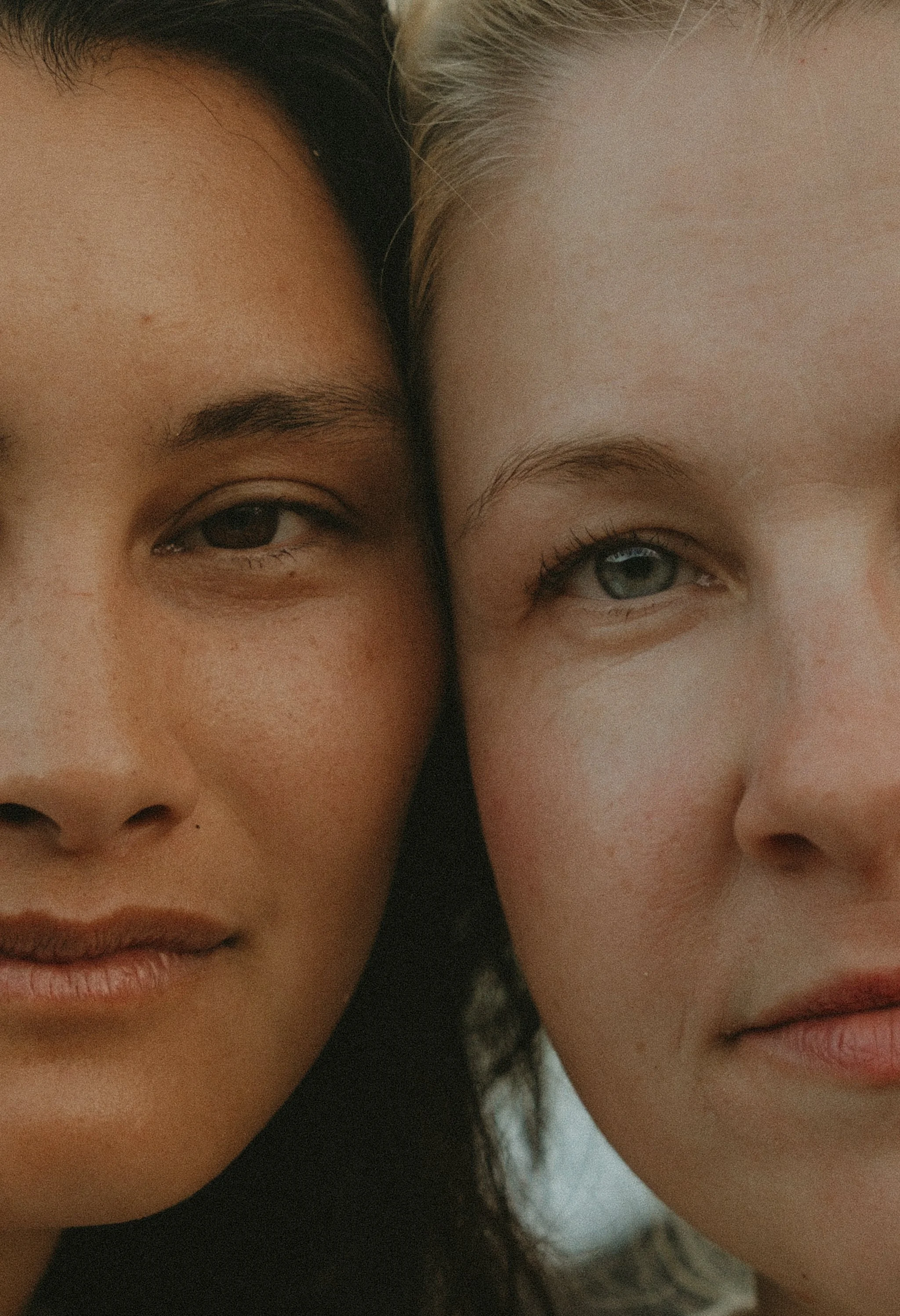 Close-up of two women’s faces, one with dark hair and darker skin, the other with light hair and lighter skin, showing a friendly expression.