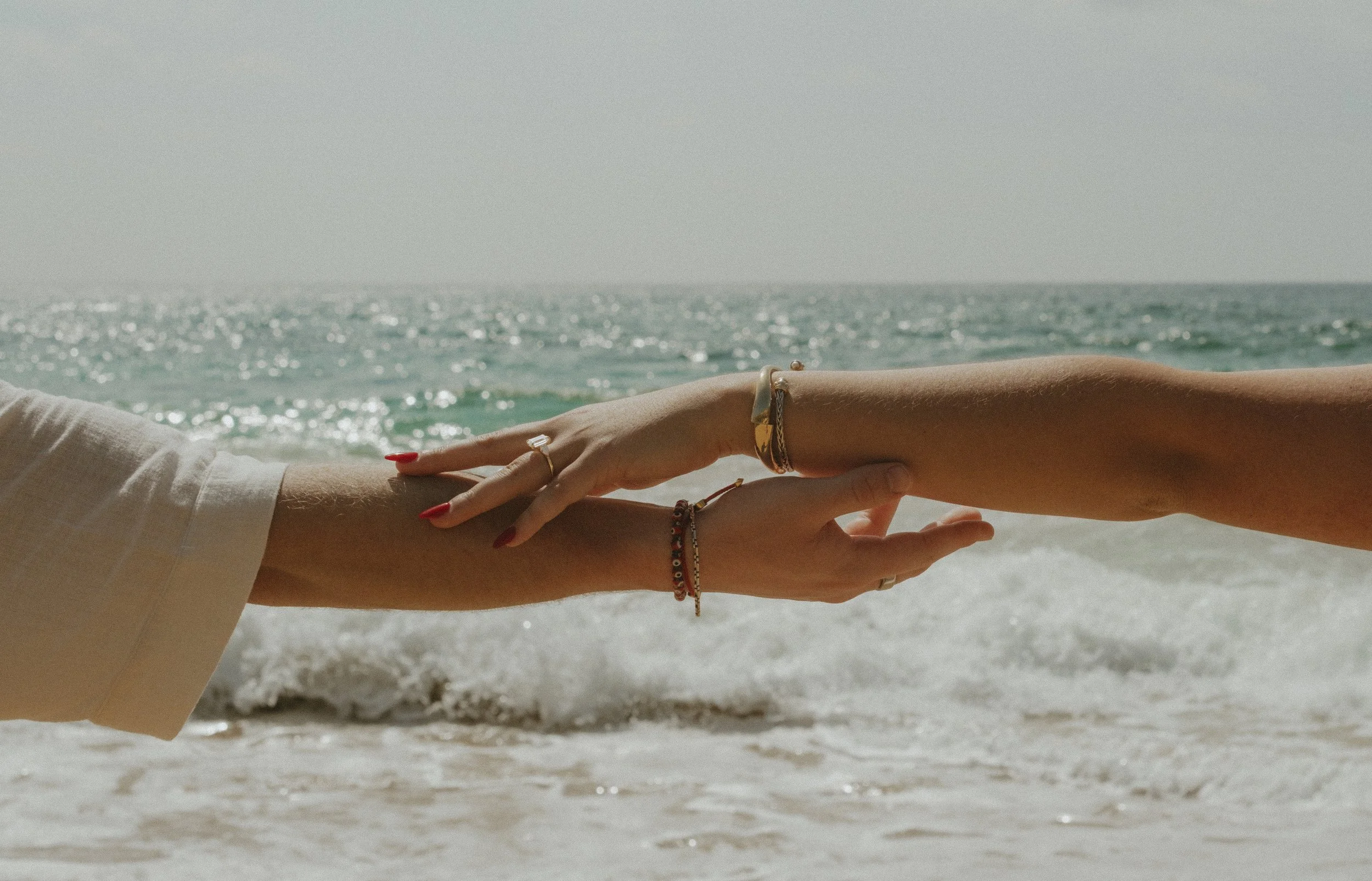 Two hands reaching out and touching each other over the ocean at the beach.