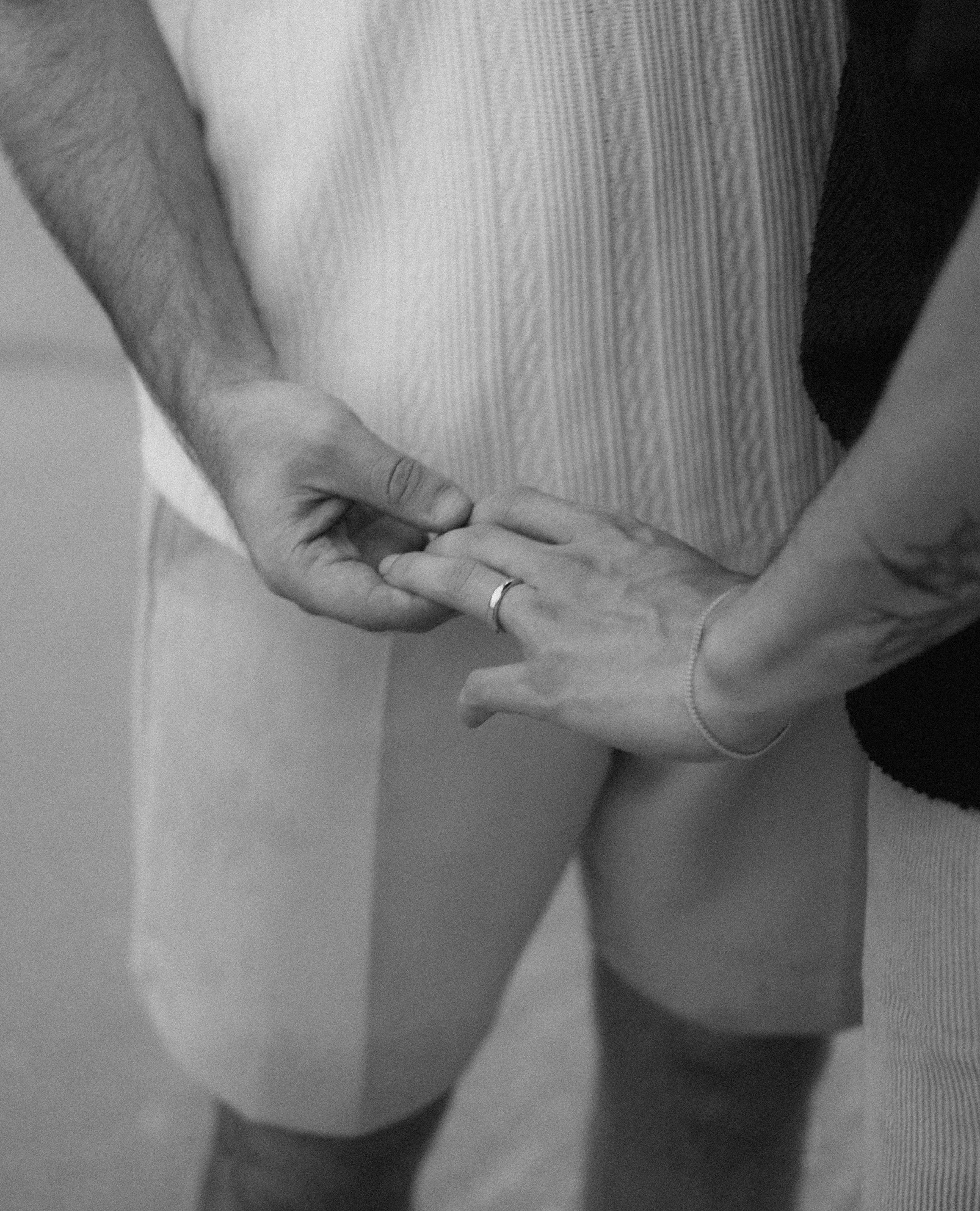 A close-up of a couple holding hands, with one person wearing a wedding ring, focusing on the hands and part of their torsos.