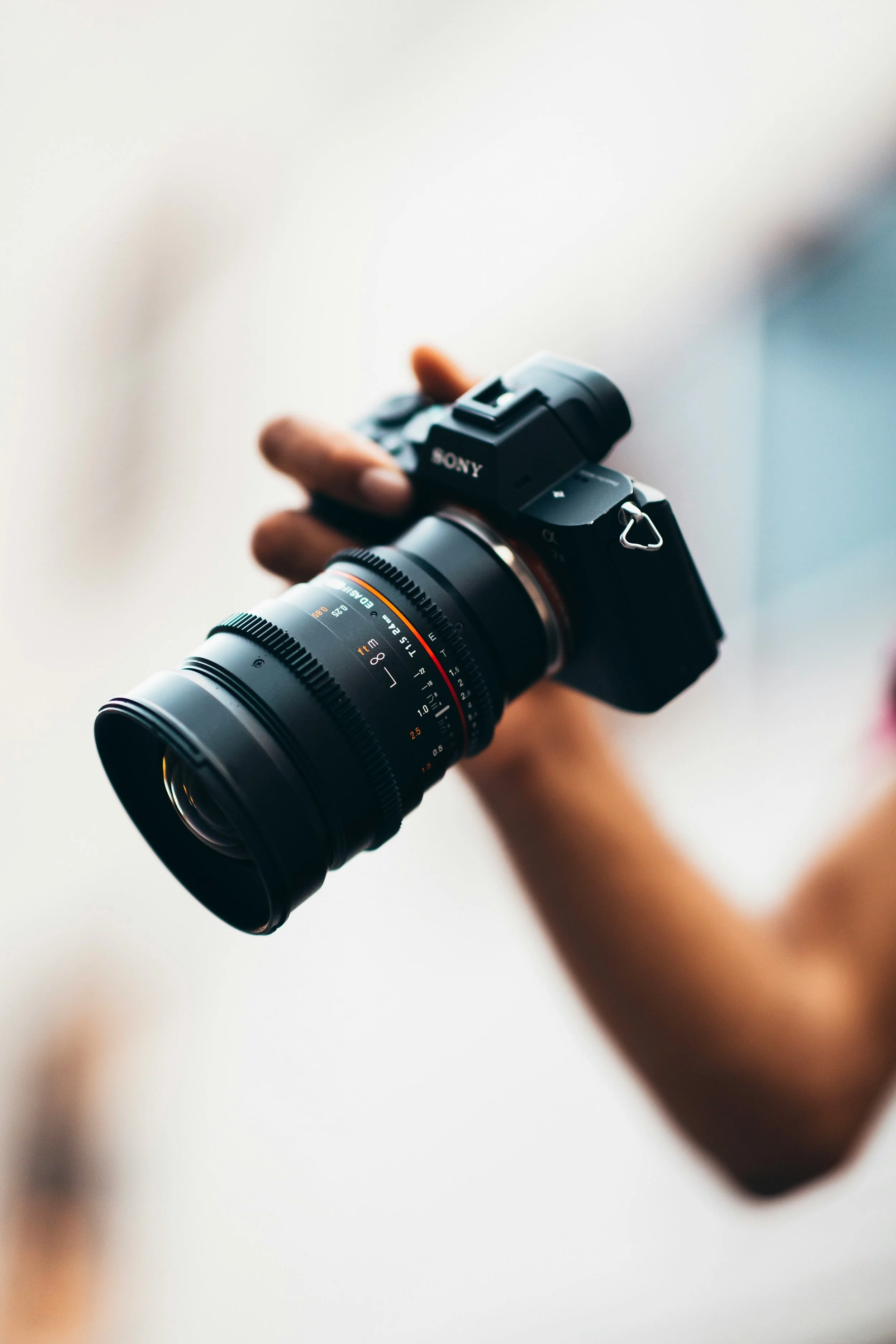 Close-up of a videographer holding a black Sony camera with a large zoom lens.