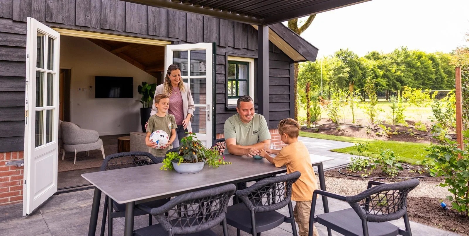 Gezin zit buiten op het terras te praten terwijl de kinderen binnen spelen.