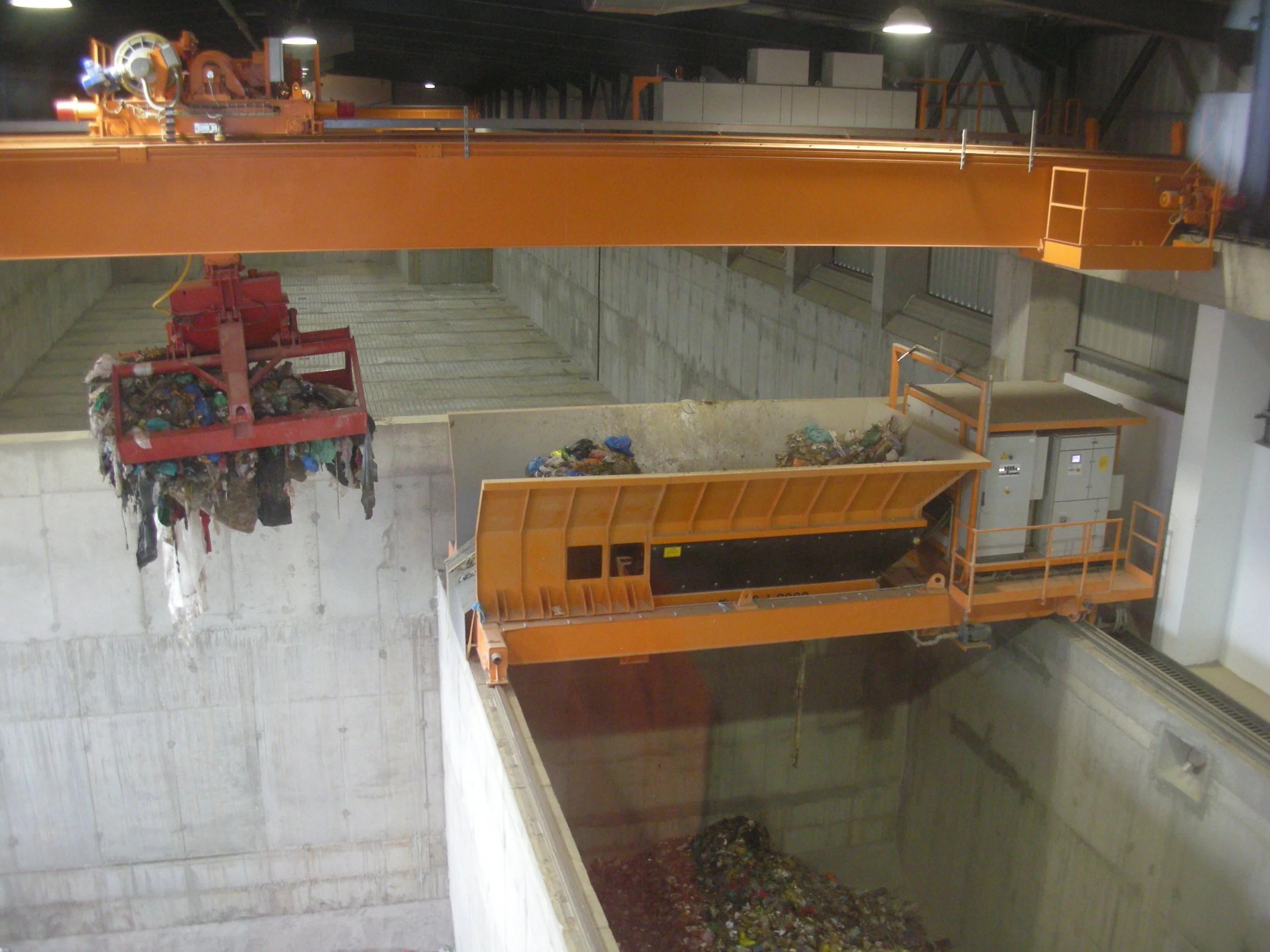 Indoor waste management facility with an overhead cane lifting mixed waste with a Rozzi grab.