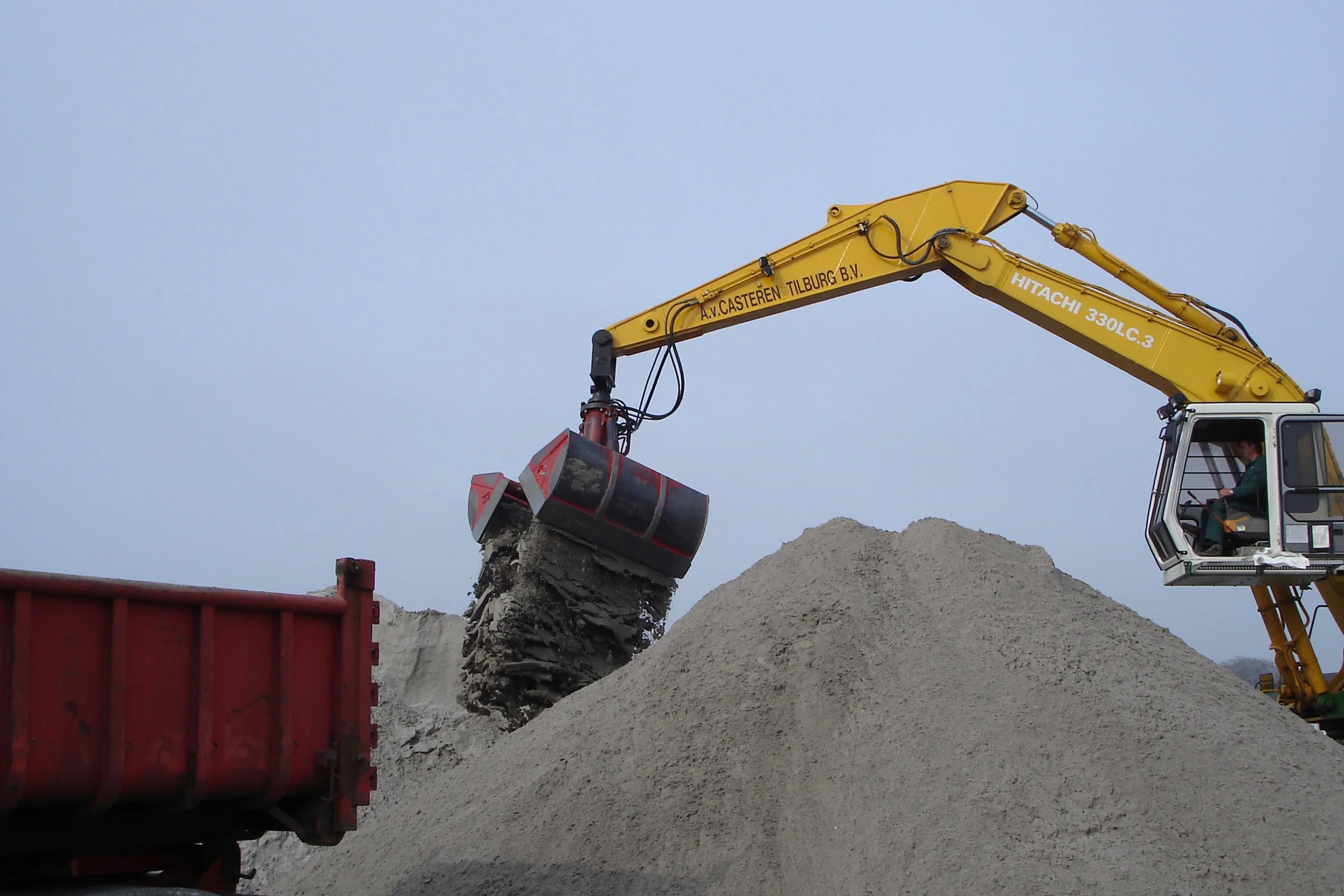	
Close-up of a Rozzi Clamshell grab attached to a yellow excavator on a construction site.