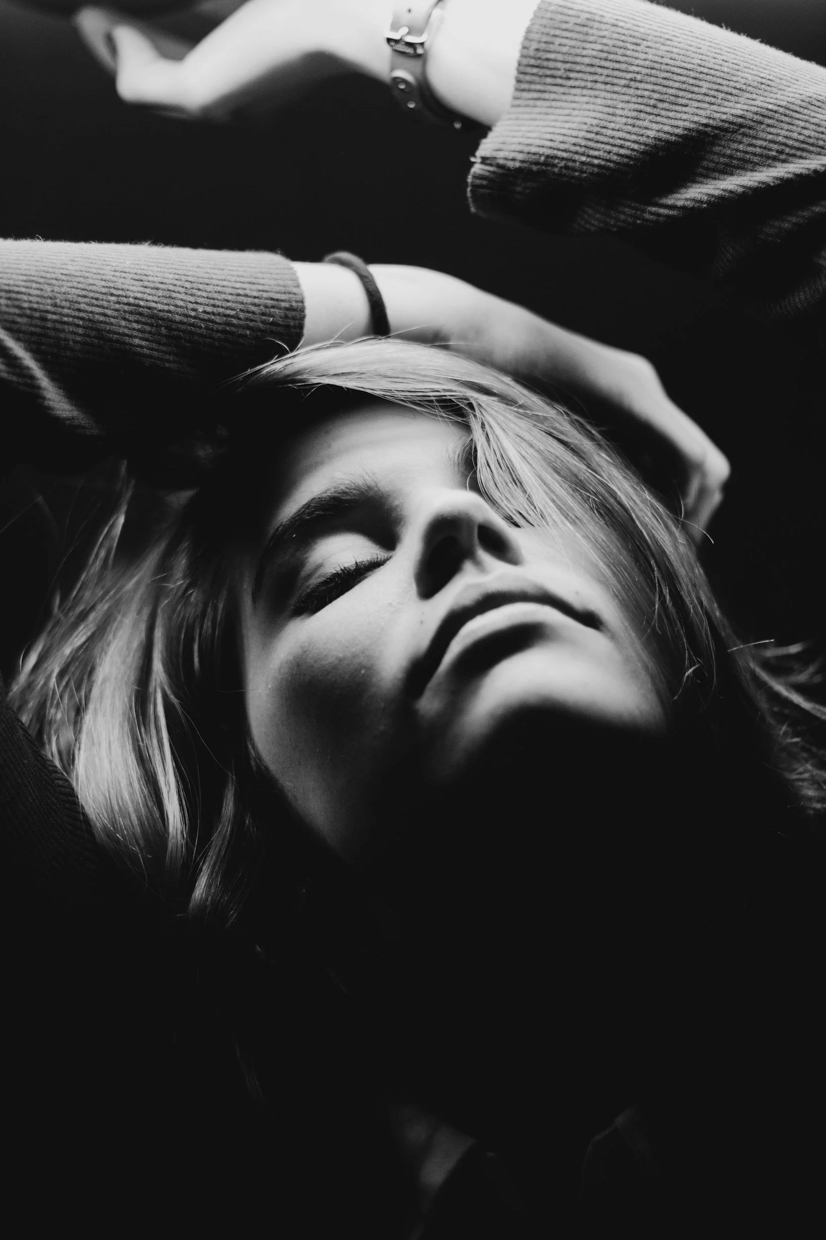 A black and white photograph of a woman lying down with her eyes closed and her hand touching her forehead, appearing relaxed or contemplative.
