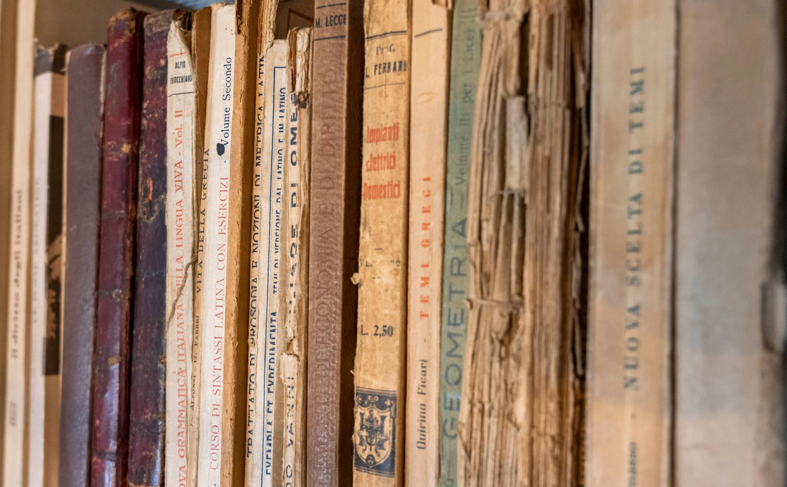 Ripiani con libri antichi e usurati, alcuni con copertine di carta ingiallite e federe tinscate.