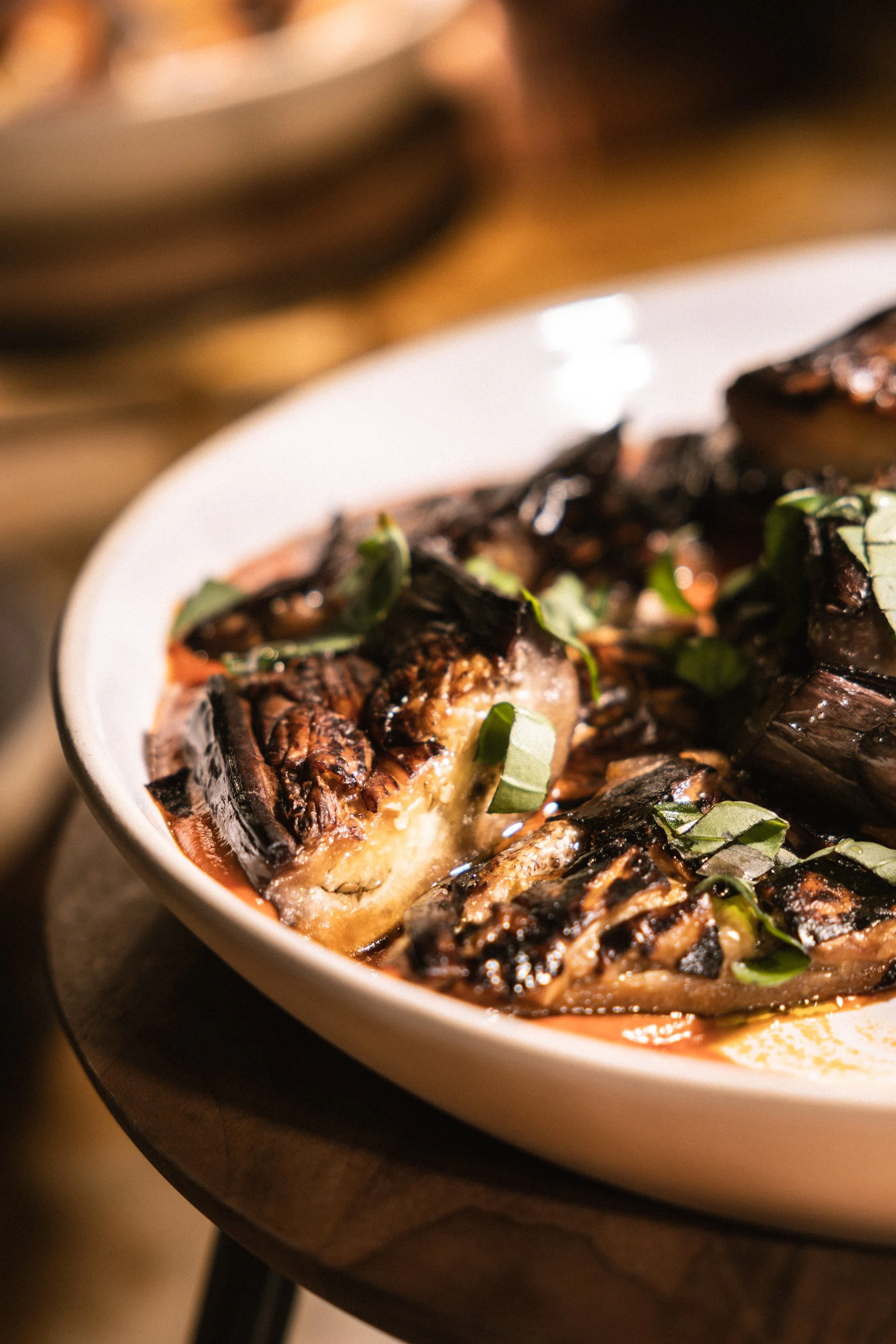 Close-up of grilled eggplant slices topped with chopped green herbs, served in a white dish.