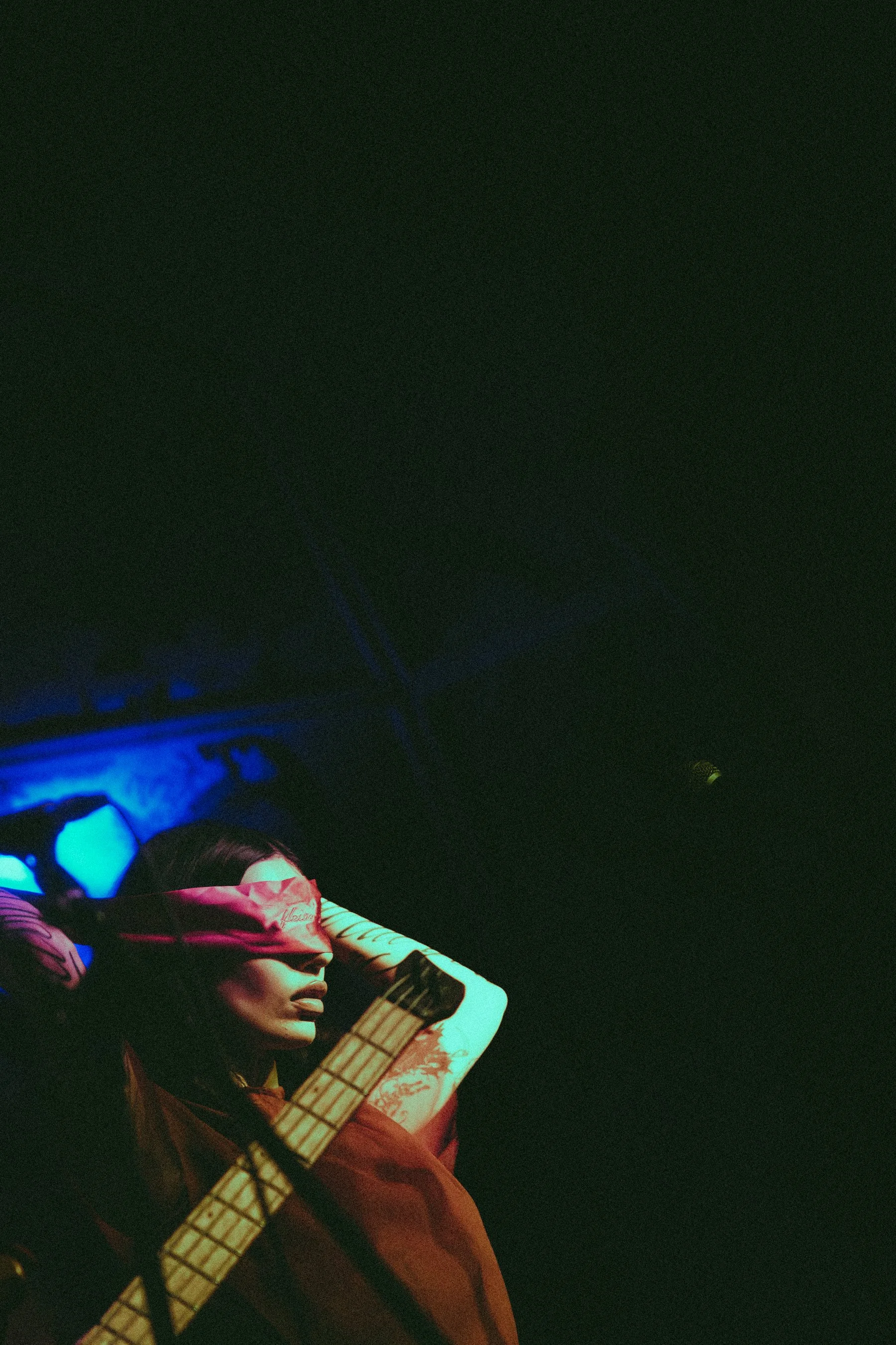 A performer on stage with a scarf covering their eyes, illuminated by purple and blue stage lights.