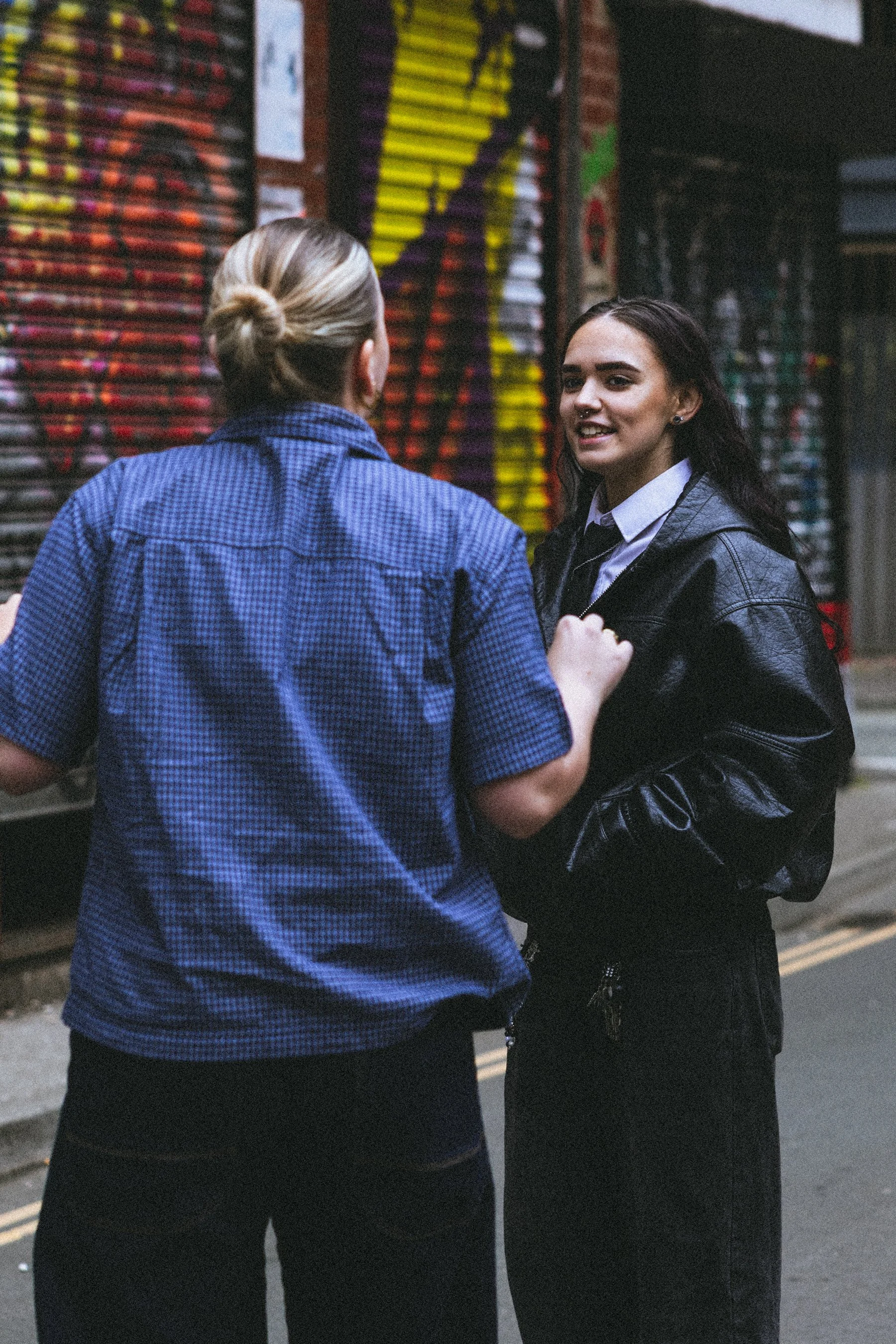 Two people having a conversation outdoors at night, near a wall with colourful graffiti.